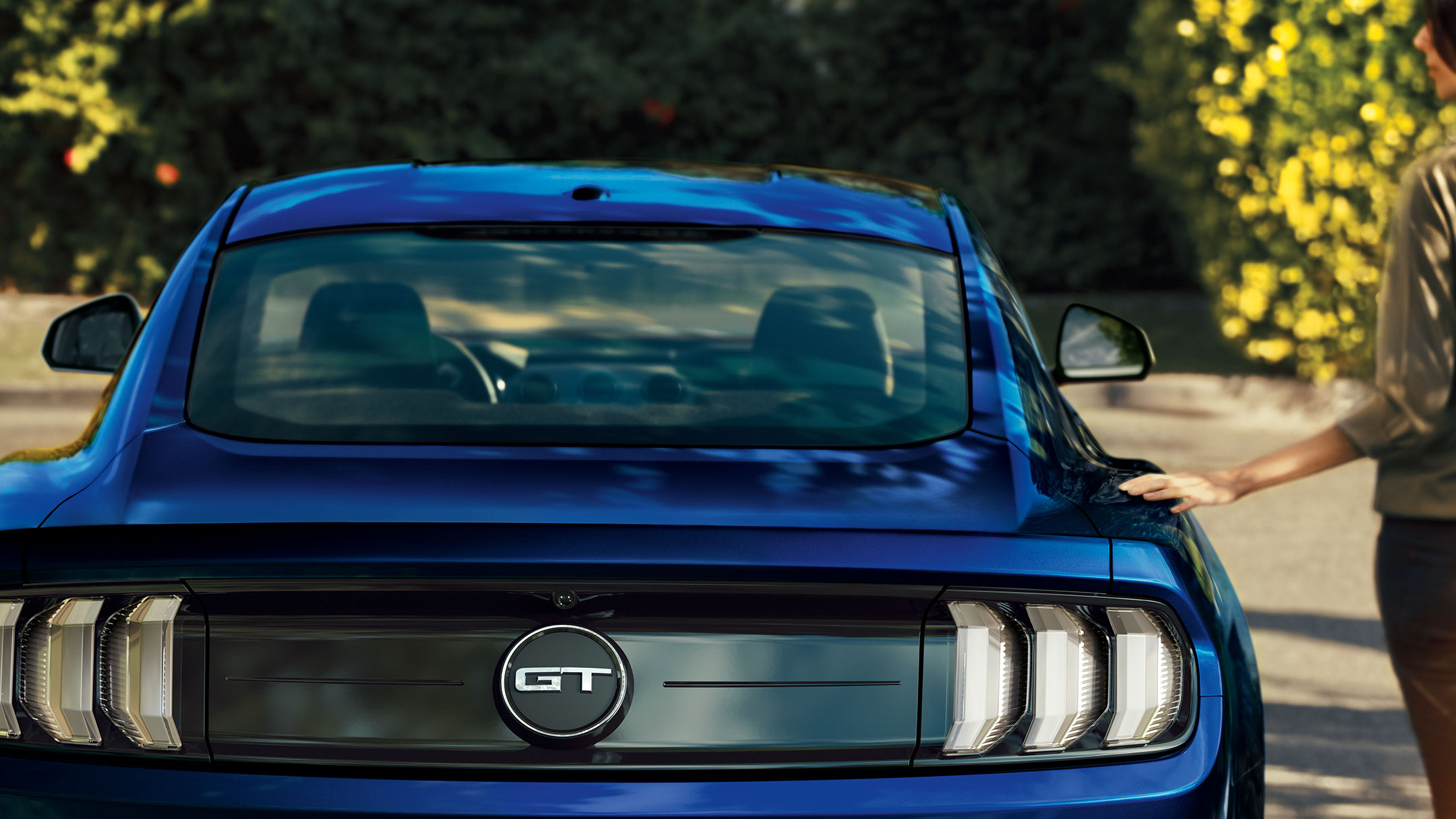 Ford Mustang GT couleur bleue Vue arrière, avec une femme se tenant à côté du véhicule.