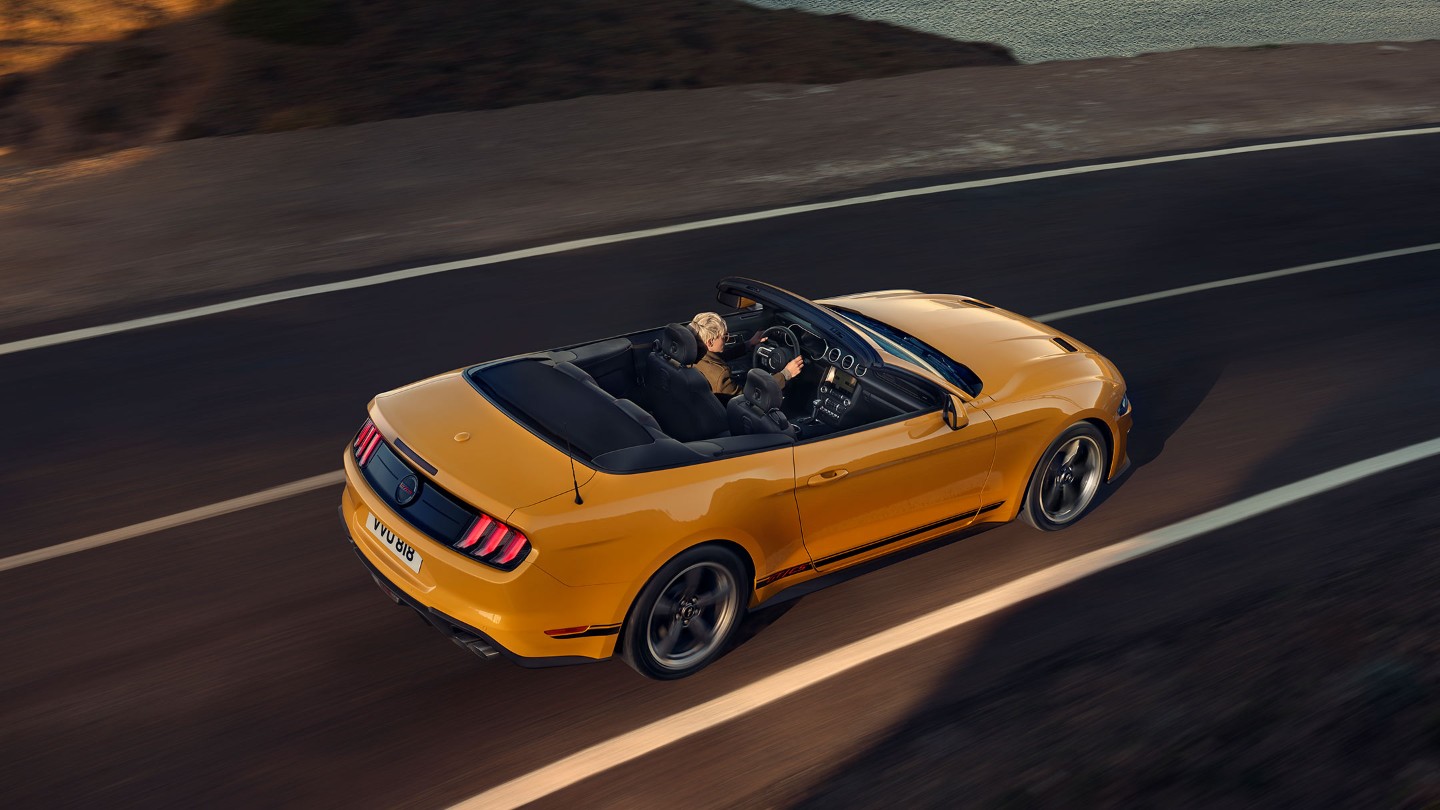 Ford Mustang California couleur orange. Vue arrière aux trois quarts, roulant sur une route.