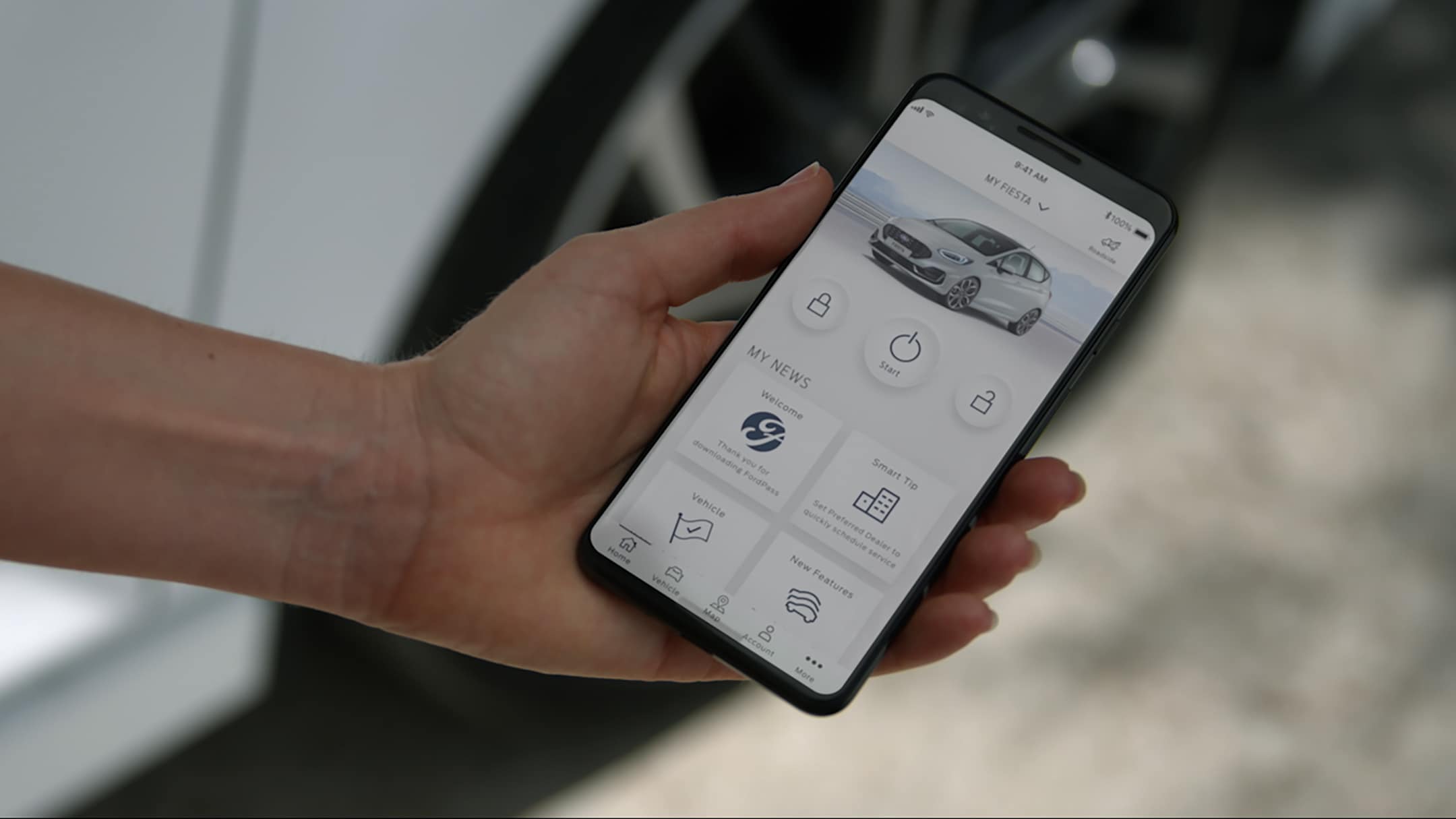 Application FordPass sur un smartphone, devant une Ford Fiesta ST blanche.