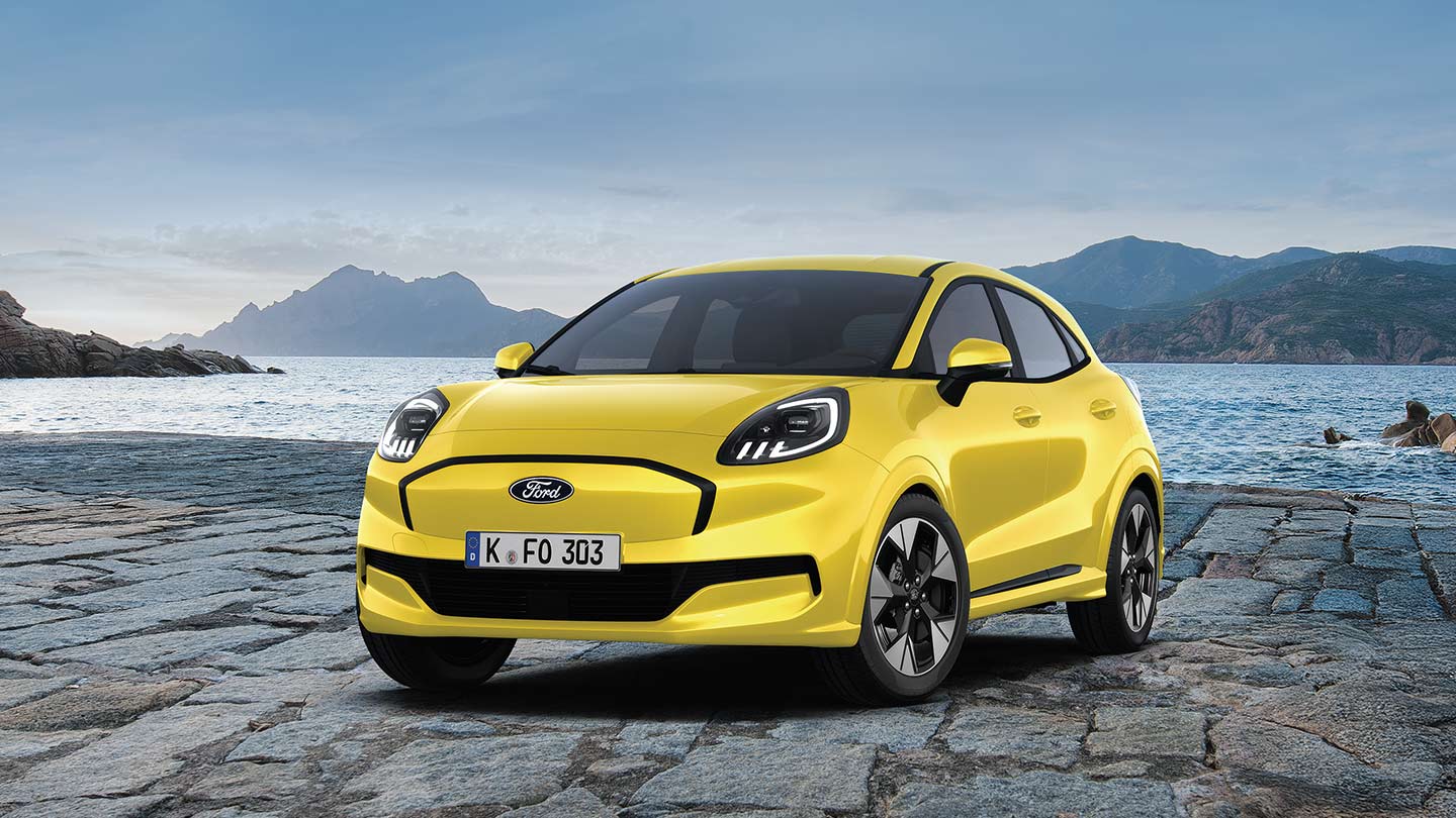 Le Ford Puma Gen-E dynamique et électrique en rouge, photographiée devant un arrière-plan pittoresque d’eau et de montagnes.