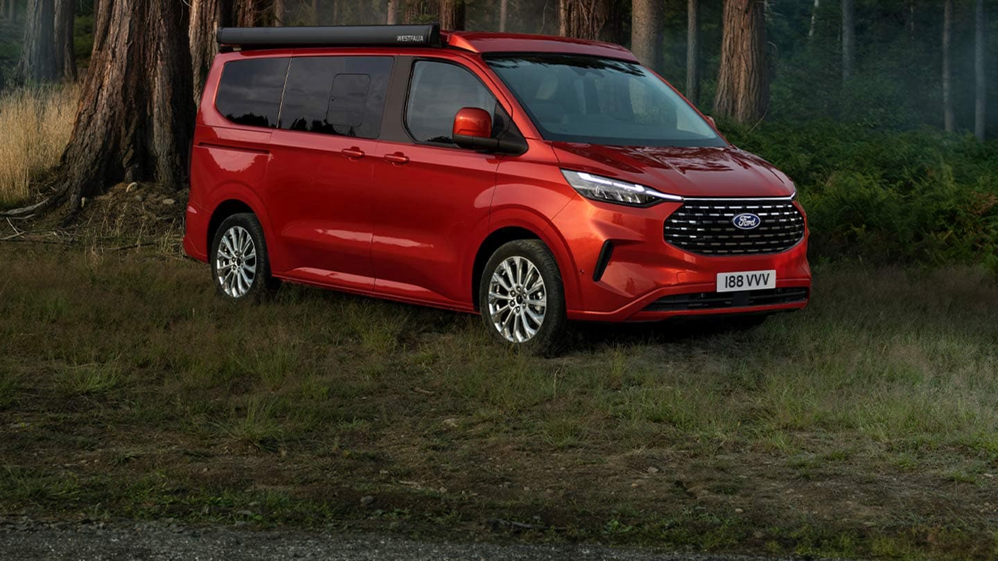 Ford Nugget rouge, garé sur une pelouse dans la forêt.