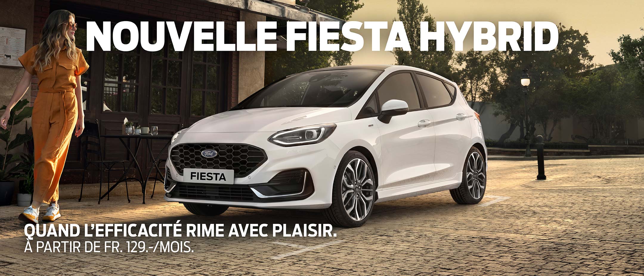 Ford Fiesta couleur blanche. Vue de face aux trois quarts, stationnant devant un restaurant avec une femme au premier plan.