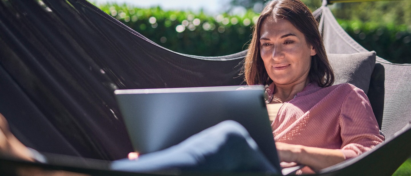 Une personne utilise un ordinateur portable tout en se relaxant dans un hamac en plein air.