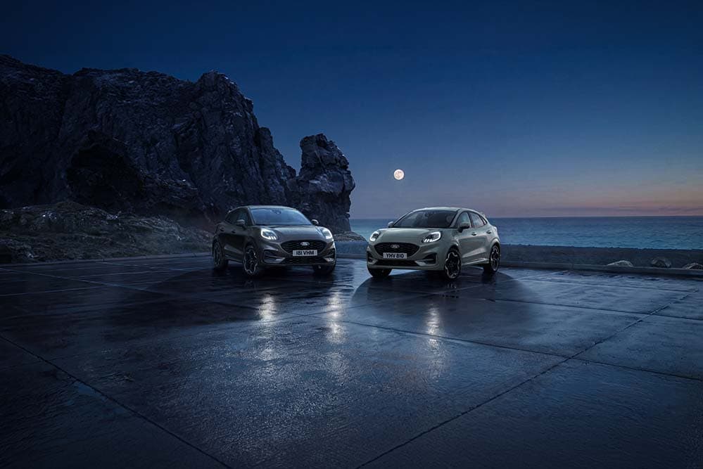 Deux Ford Puma stationnées la nuit au bord de la mer sous la pleine lune.