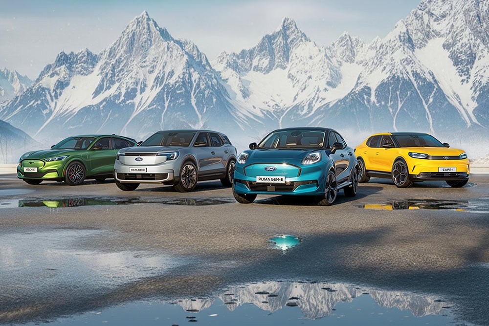 Quatre modèles Ford colorés sont côte à côte sur sol mouillé devant des montagnes enneigées.