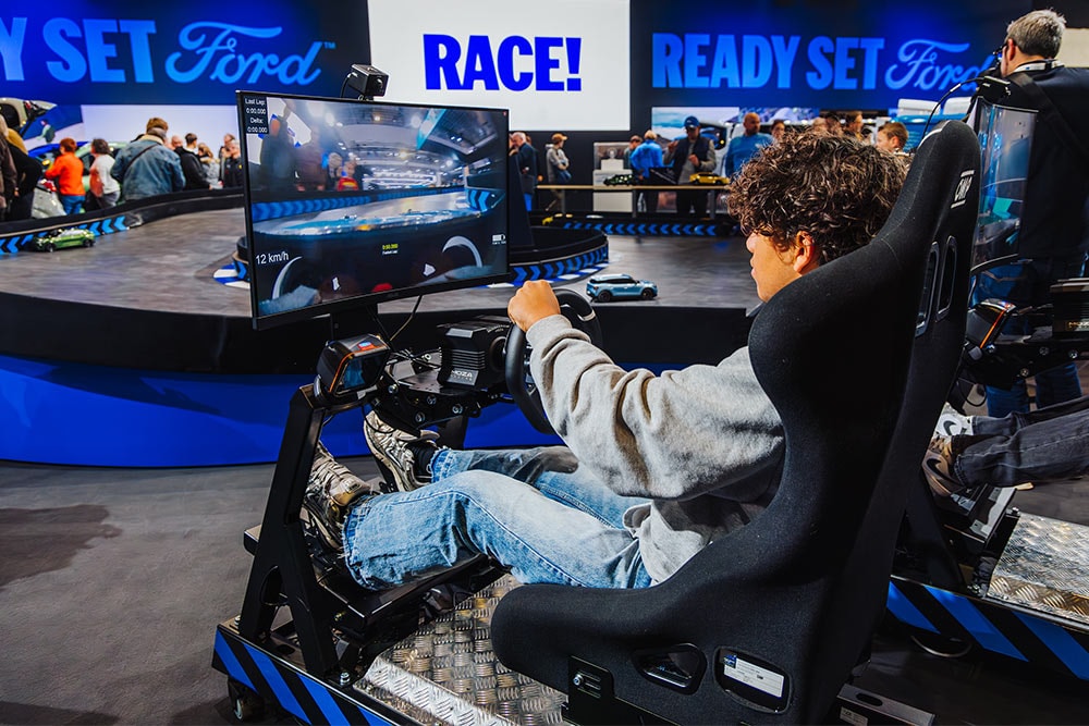 Un visiteur joue sur un simulateur de course virtuel sur un stand Ford à l'éclairage moderne.