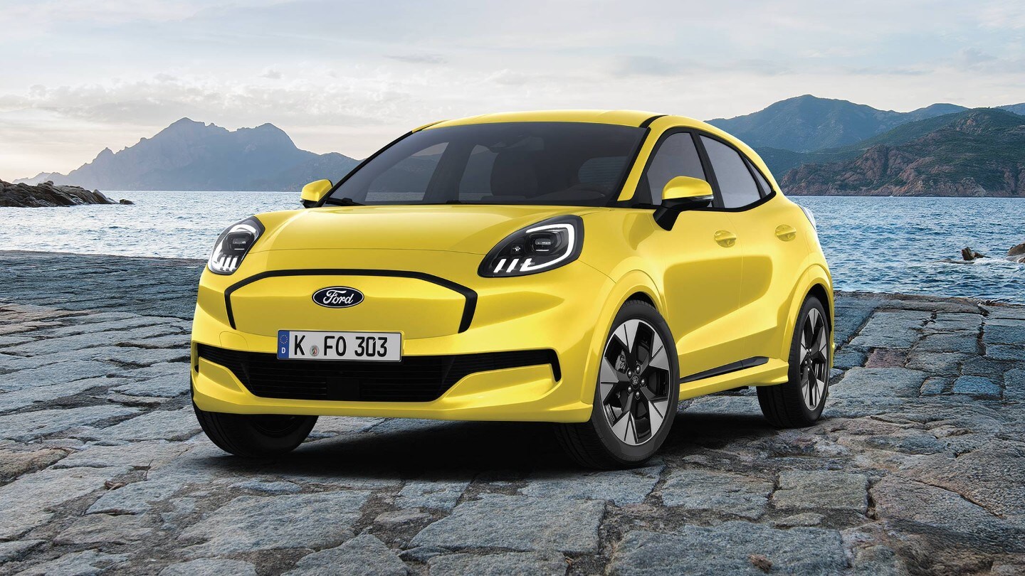Le Ford Puma Gen-E dynamique et électrique en rouge, photographiée devant un arrière-plan pittoresque d’eau et de montagnes.