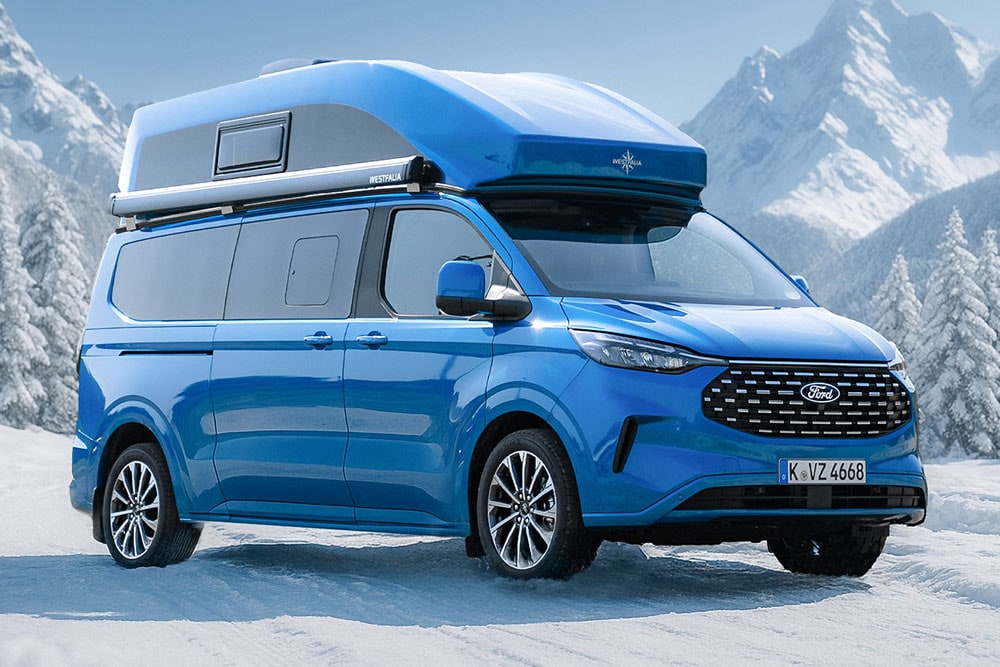 Vue avant aux trois quarts d’un Ford Nugget bleu avec toit surélevé, garé dans la neige devant un paysage de montagne.