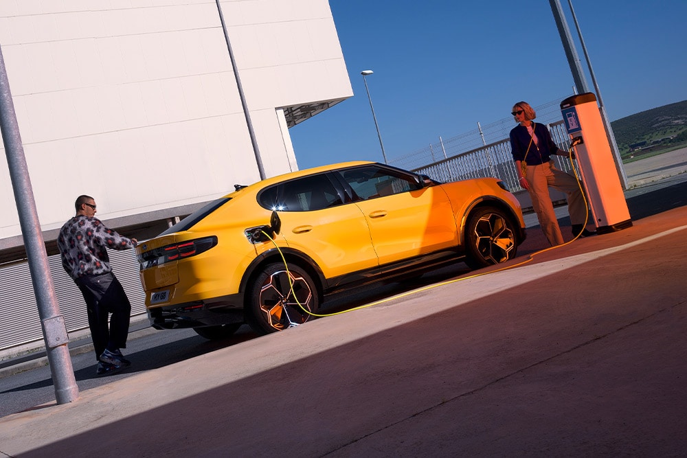 Des personnes rechargent une Ford Capri électrique jaune sur une borne publique. 