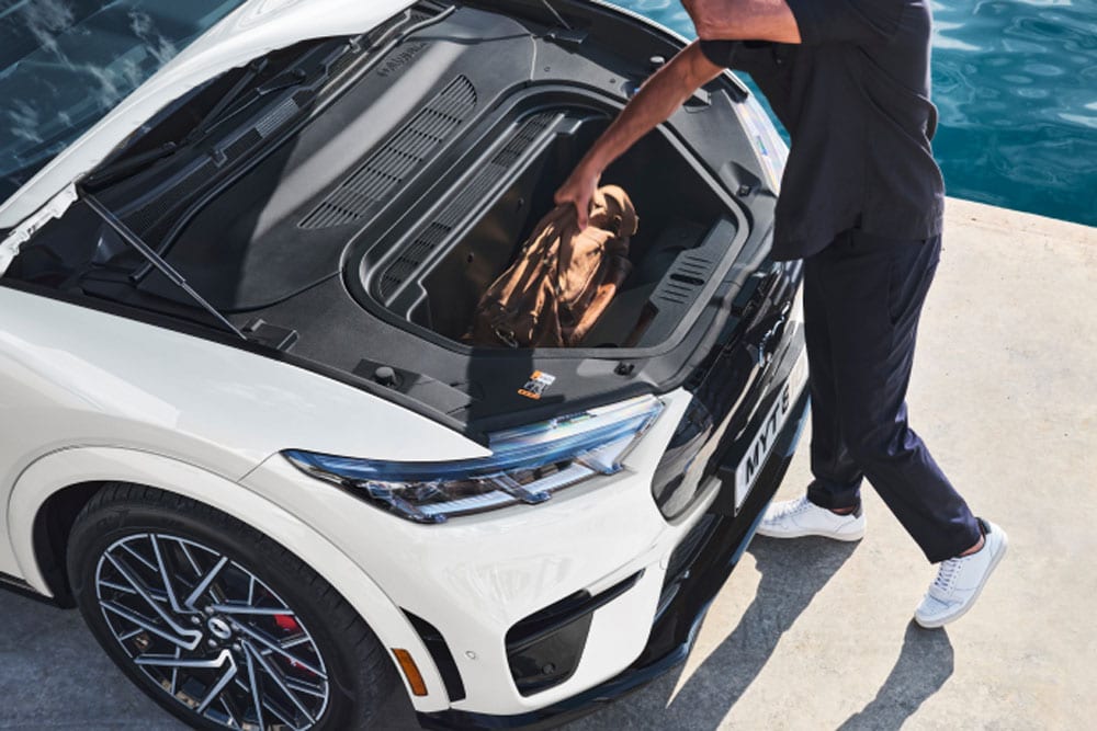 Une personne met un sac de voyage dans le coffre d’une Ford Mustang Mach-E électrique de couleur blanche. 