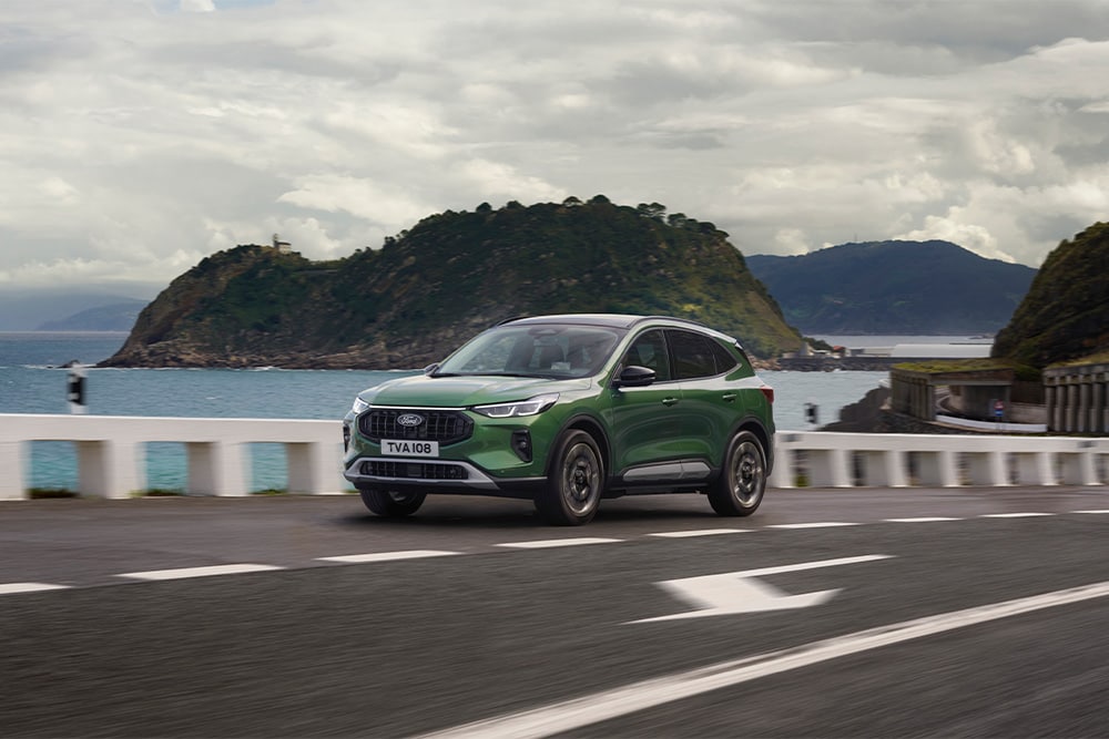 Un Ford Kuga hybride autorechargeable de couleur verte roule sur une route panoramique. 