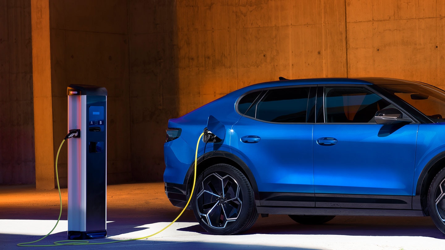 Une Ford Capri électrique bleue est branchée sur une borne de recharge. 