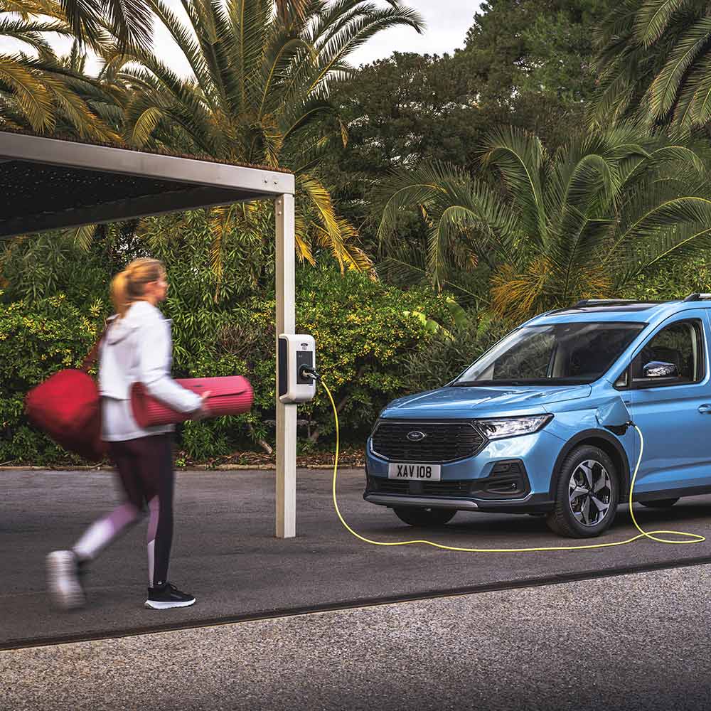 Une personne munie d’un tapis de yoga se dirige vers un Ford Tourneo Connect Plug-in-Hybrid.