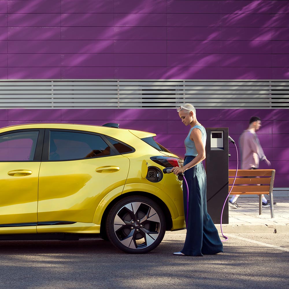 Un conducteur branche un Ford Puma Gen-E jaune sur une borne publique pour une recharge facile.
