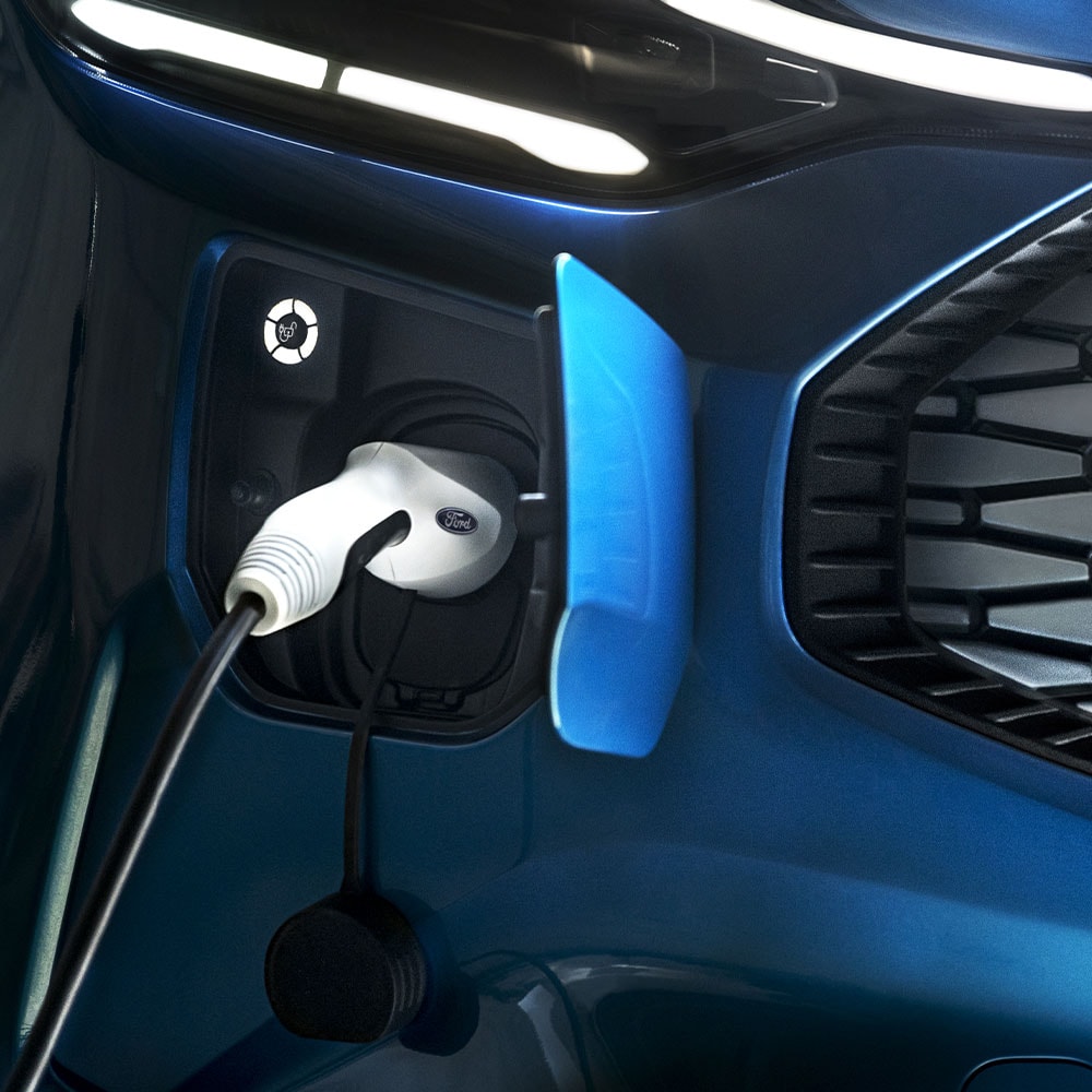 Une borne de recharge pour voitures électriques avec un chargeur connecté pour véhicules électriques devant un véhicule Ford bleu.