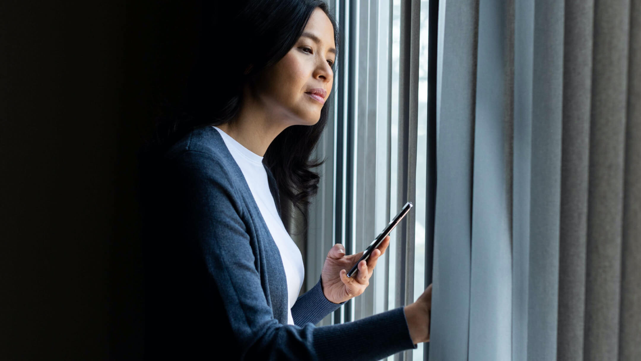 Femme tenant un smartphone et regardant par la fenêtre