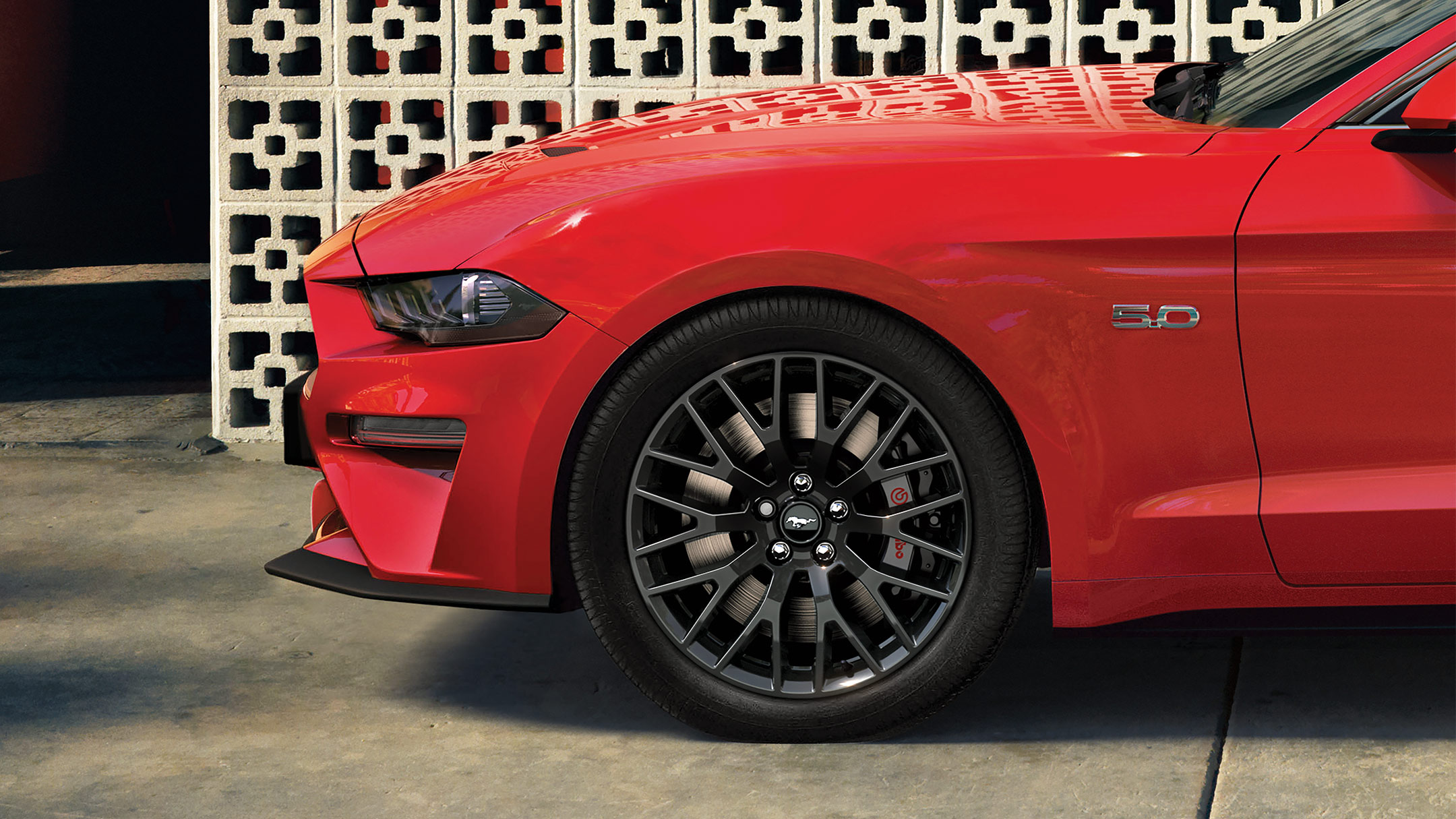 Ford Mustang couleur rouge. Vue latérale de l’avant, stationnant devant un mur de pierre décoré