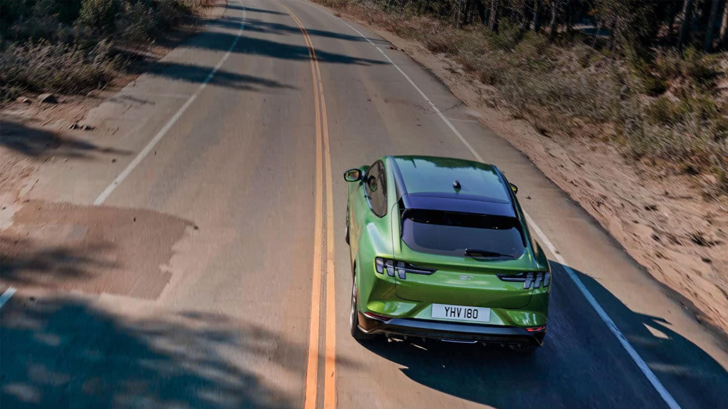 Une Ford Mustang Mach-E GT de couleur verte roule sur une route de montagne bordée d’arbres.