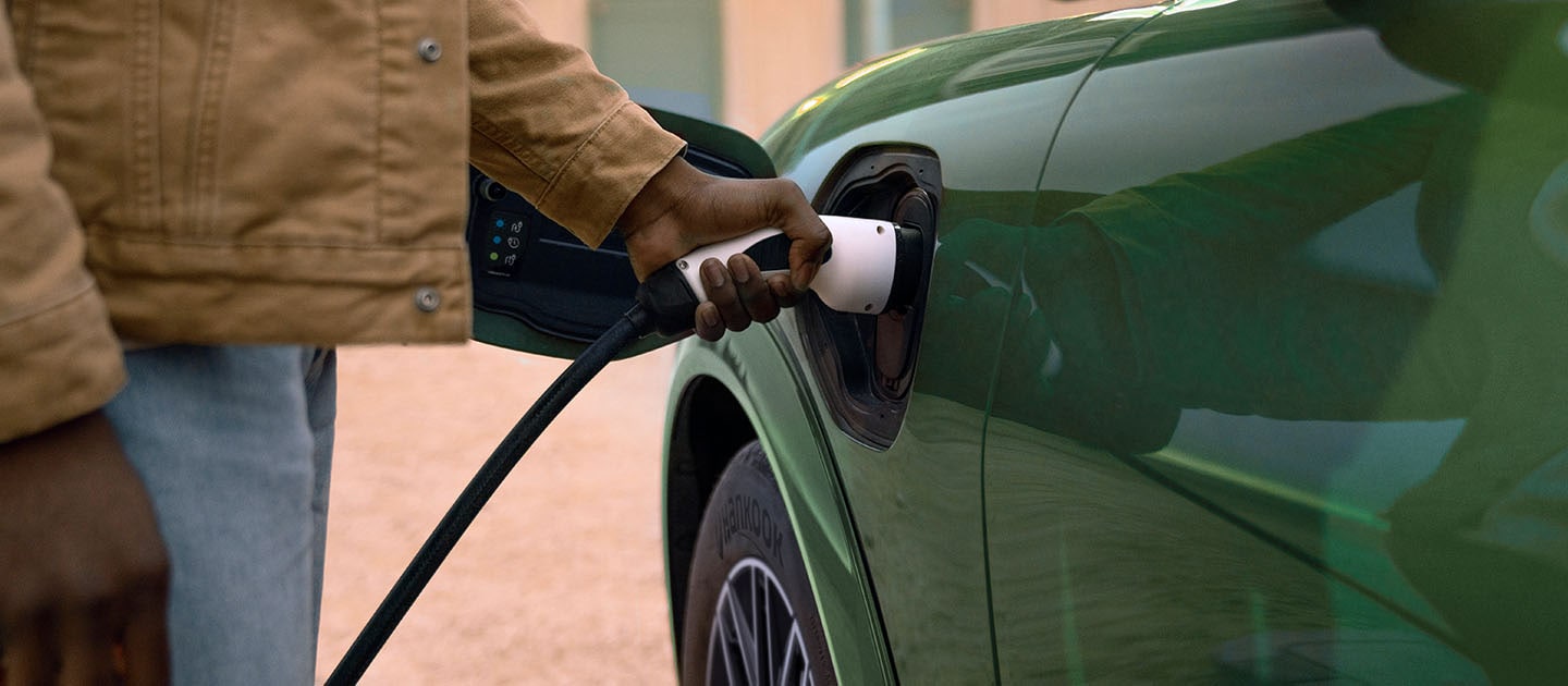 Personne vêtue d’une veste crème et branchant un câble de recharge sur sa Ford Mustang Mach-E électrique de couleur verte.