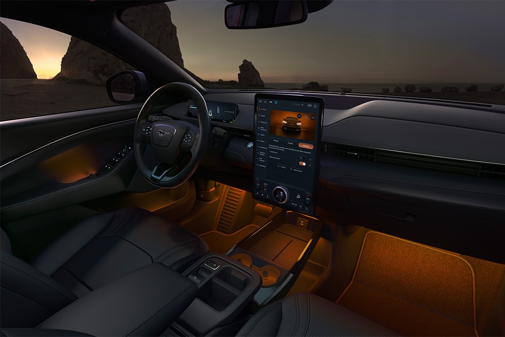Ford Mustang Mach-E la nuit, avec l’écran tactile SYNC 4 de 15.5 pouces et l’éclairage d’ambiance à LED réglé sur la couleur orange.