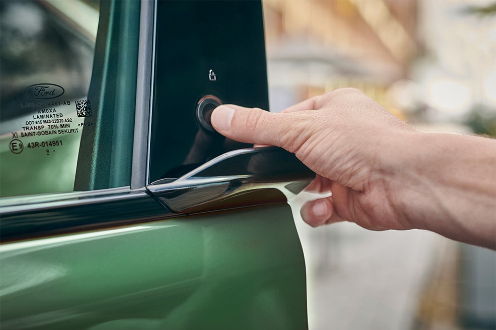 Une main appuie sur le bouton de la portière d’une Ford Mustang Mach-E de couleur verte pour l’ouvrir.