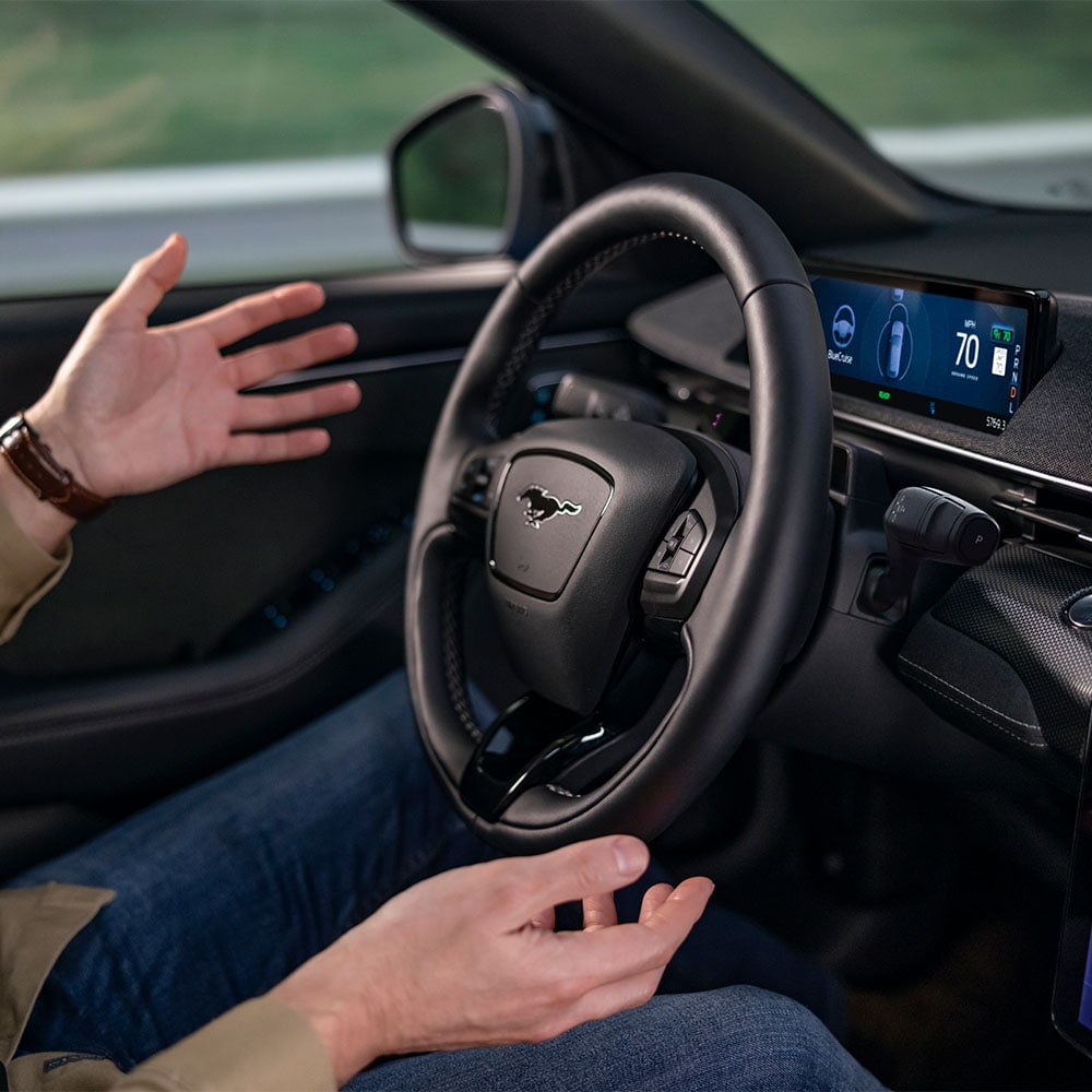 Les mains du conducteur à distance du volant de la Mustang Mach-E, illustrant la technologie BlueCruise pour la conduite autonome.