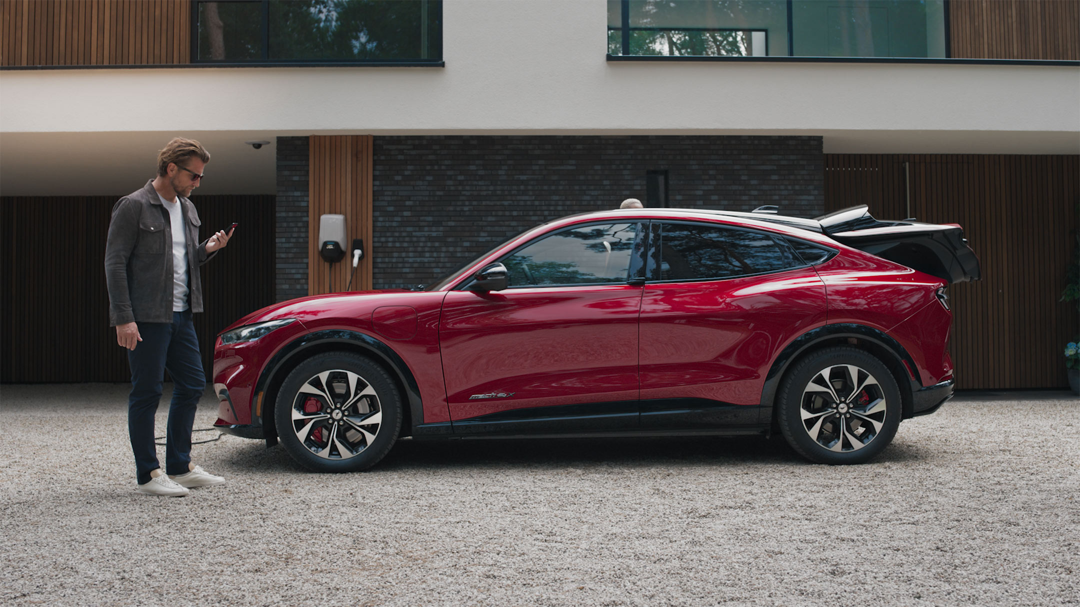 Un homme avec un smartphone se tient devant une Mustang Mach-E