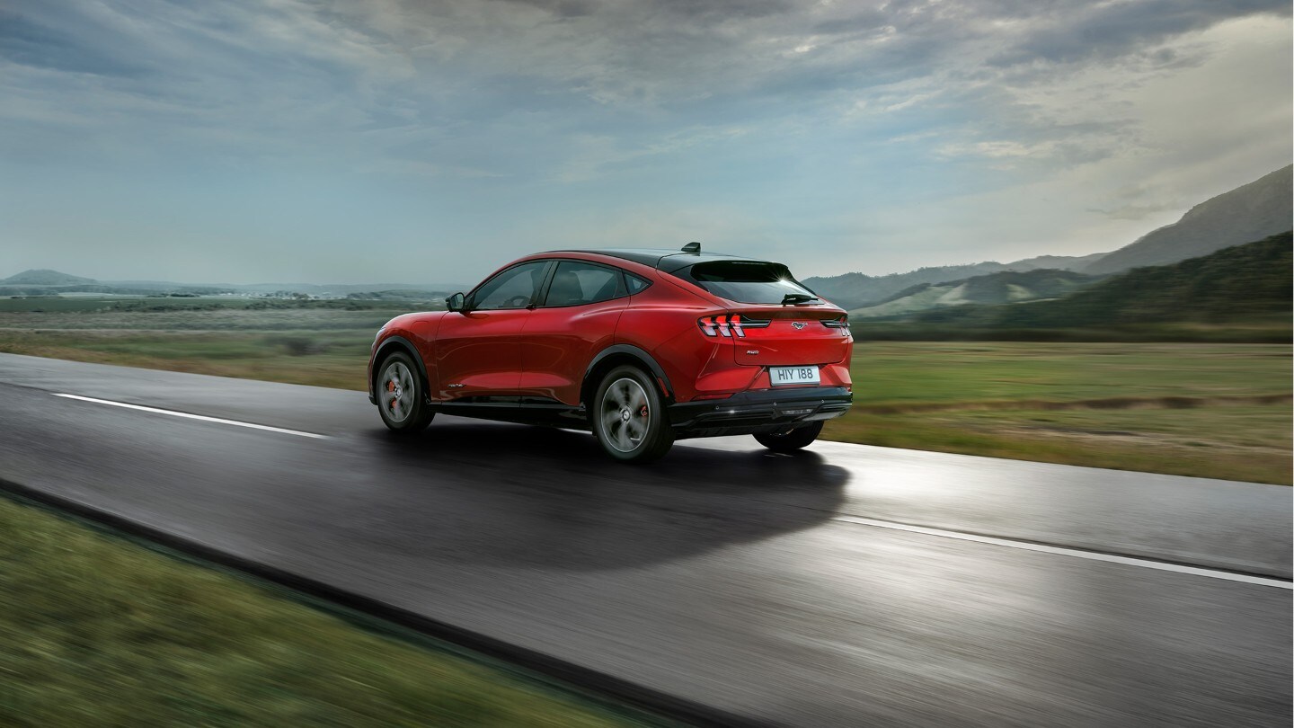 Ford Mustang Mach-E couleur rouge. Vue arrière aux trois quarts. Conduite sur une route de campagne