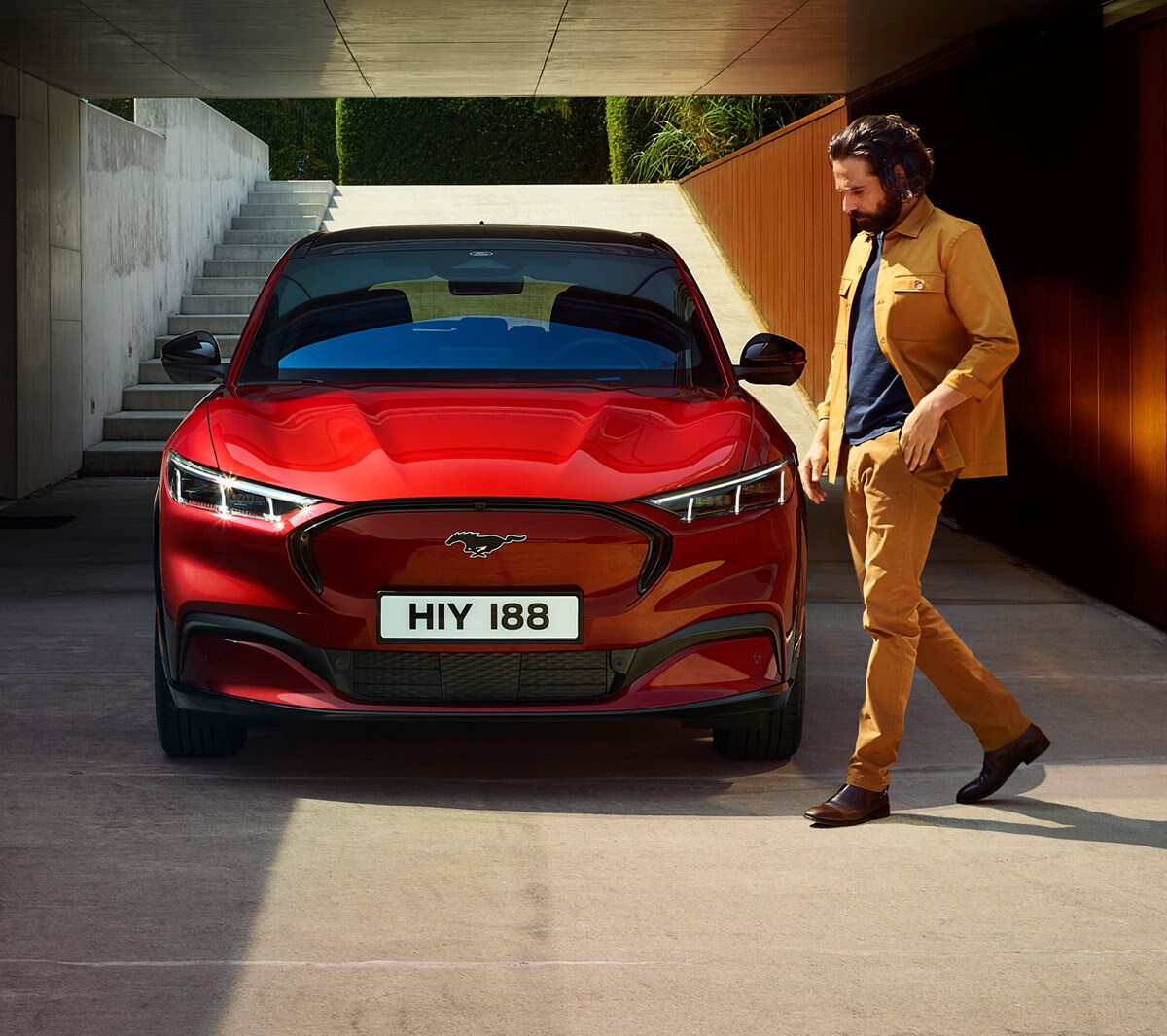 Ford Mustang Mach-E couleur rouge. Vue de face. Un homme tourne autour de la voiture