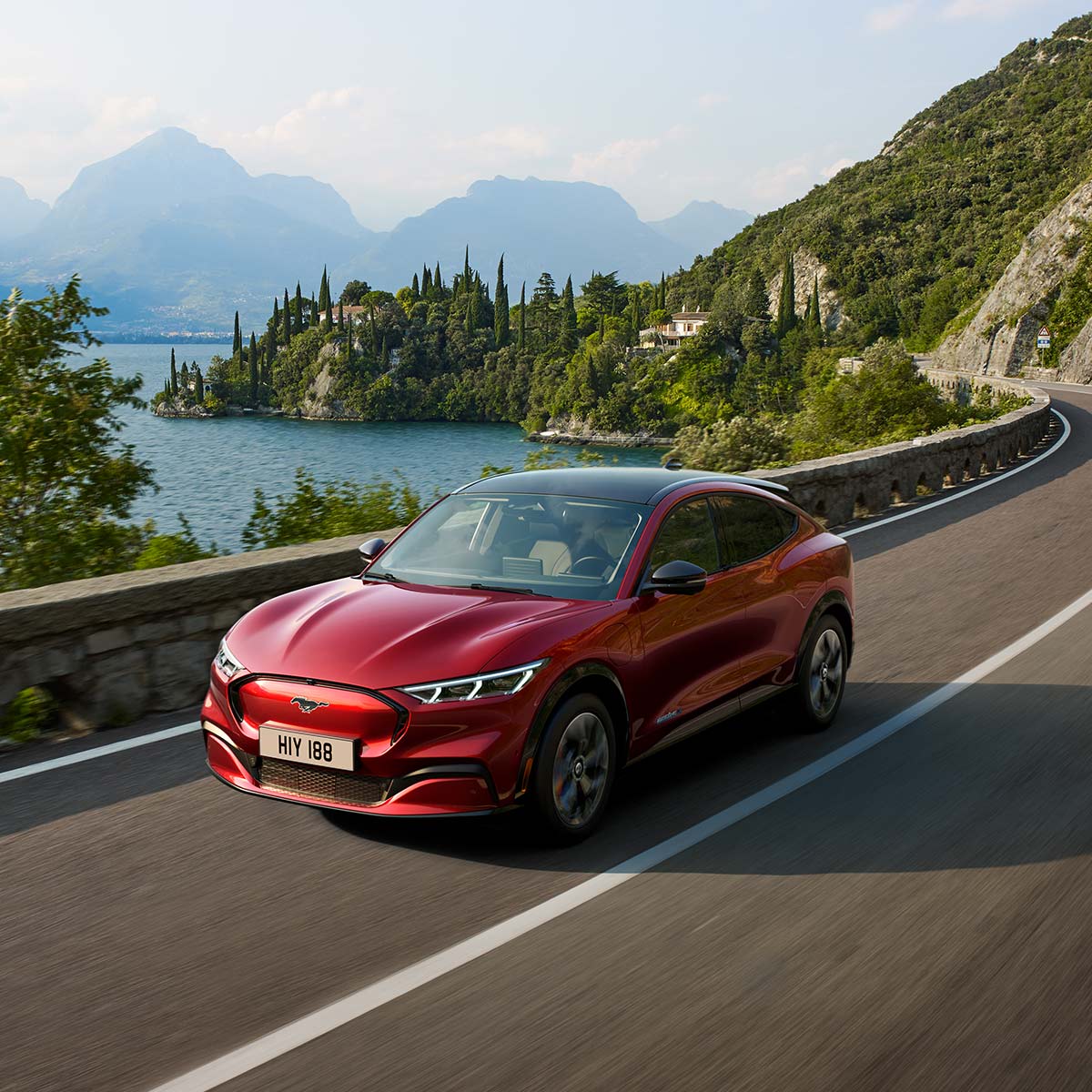 Ford Mustang Mach-E couleur rouge. Vue aux trois quarts, roulant sur une route de montagne