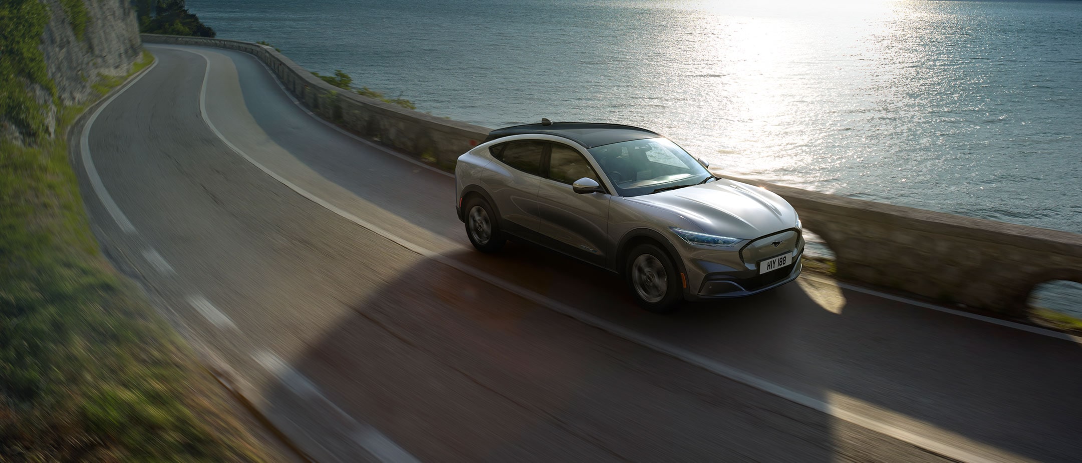 Silver All Electric Ford Mustang Mach-E driving sunny cliffs and sea