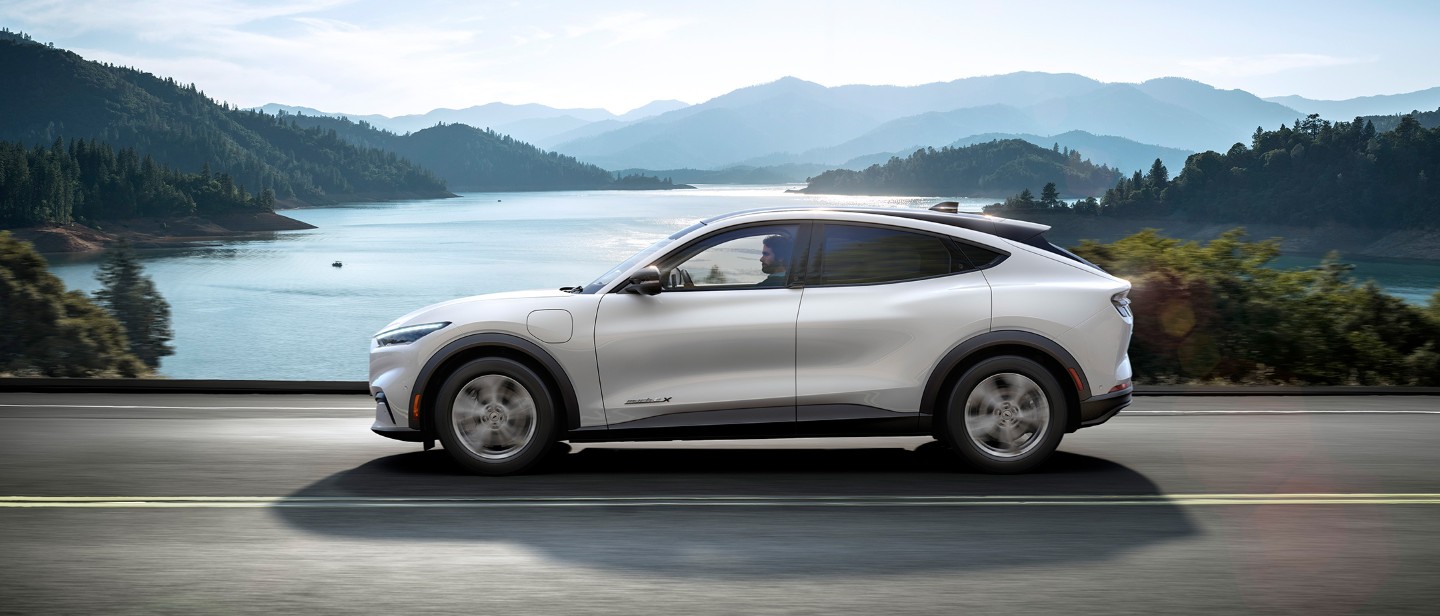 Silver All Electric Ford Mustang Mach-E driving sunny cliffs and sea