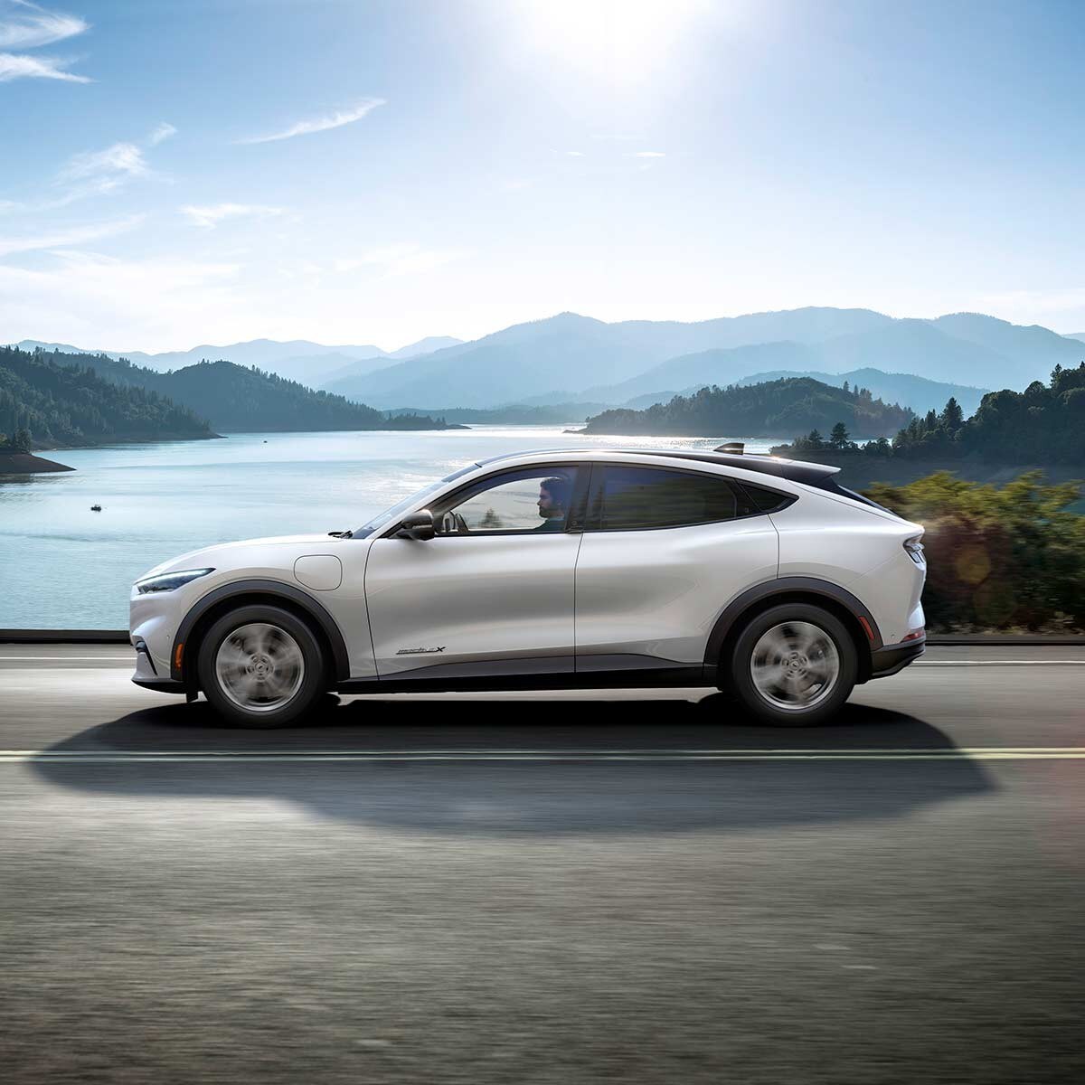 Ford Mustang Mach-E en argent vue de côté conduisant devant le lac