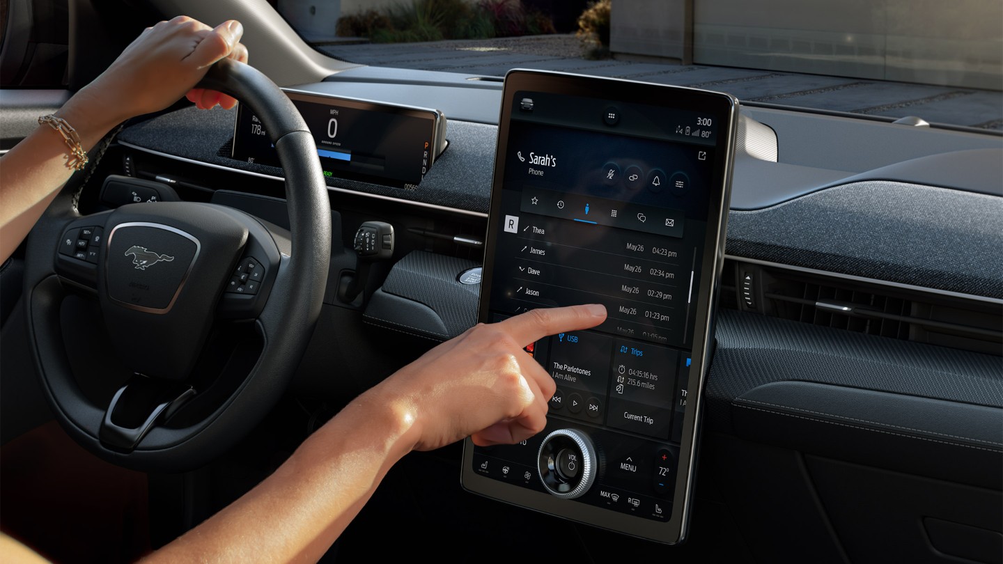 Ford Mustang Mach-E. Détail de l'utilisation de l'écran tactile Ford SYNC 4A par la main du conducteur.