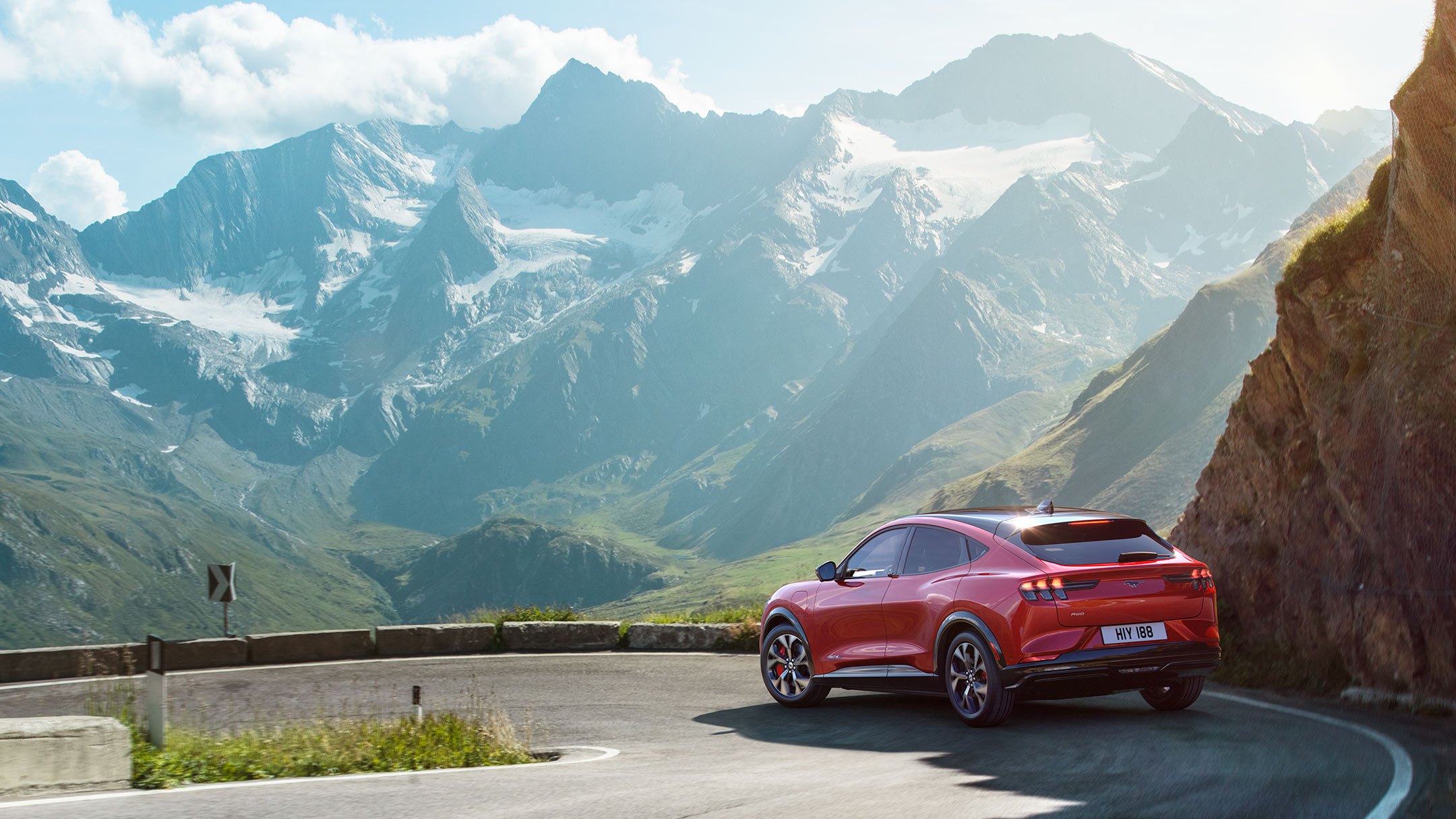 Ford Mustang Mach-E couleur rouge. Vue arrière aux trois quarts. Conduite sur une route panoramique de montagne sinueuse