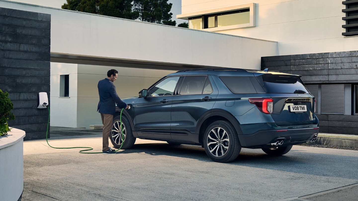 Ford Explorer Plug-In Hybrid couleur bleue. Vue arrière aux trois quarts. Recharge devant un bâtiment.