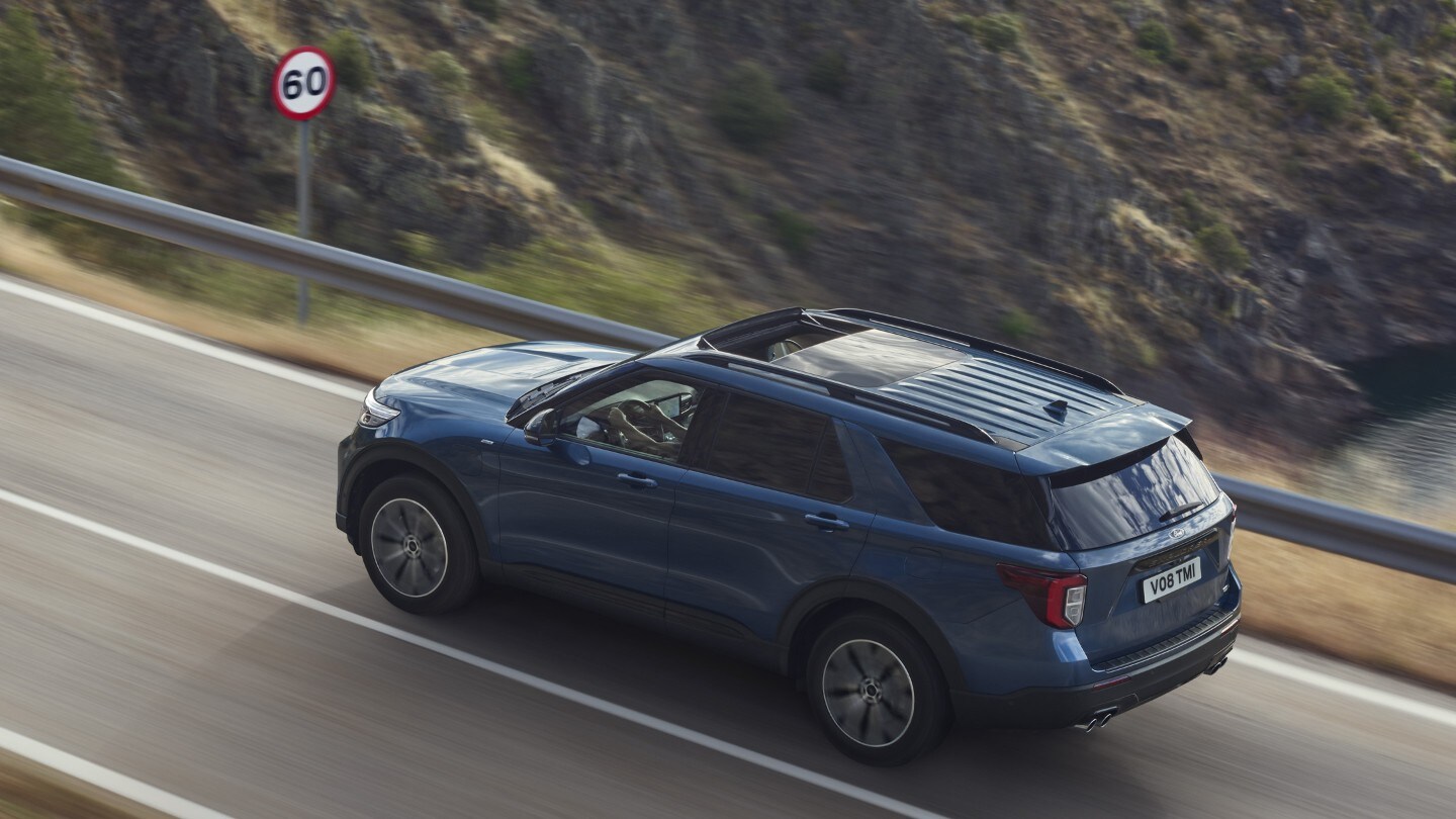 Ford Explorer Plug-In Hybrid bleu. Vue trois-quarts arrière. Conduite sur une route de montagne