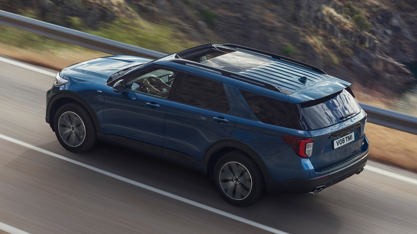 Ford Explorer Plug-In Hybrid bleu. Vue trois-quarts arrière. Conduite sur une route de montagne