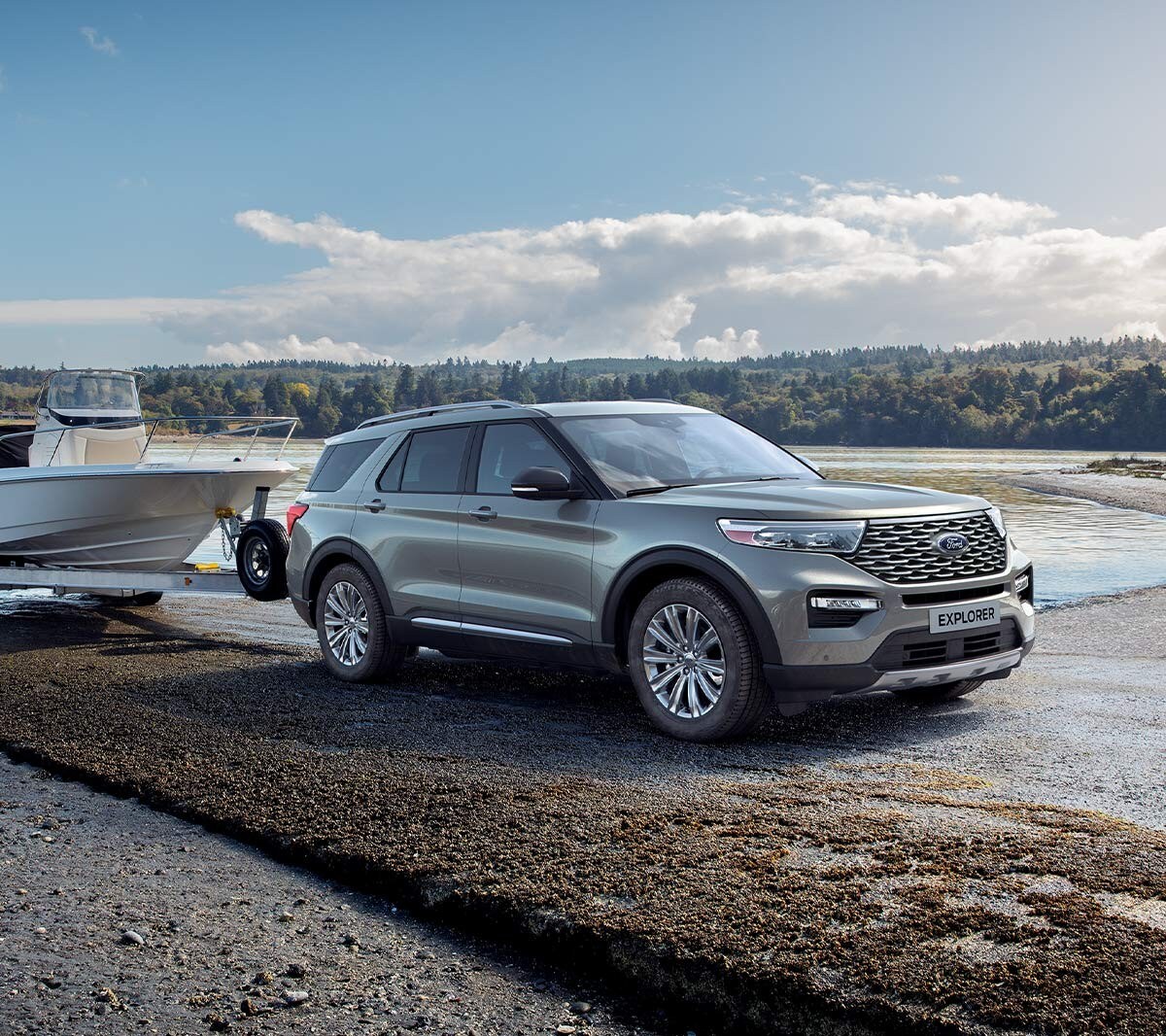 Ford Explorer Plug-In Hybrid couleur argent. Vue de face aux trois quarts. Avec une remorque à bateaux au bord d’un lac