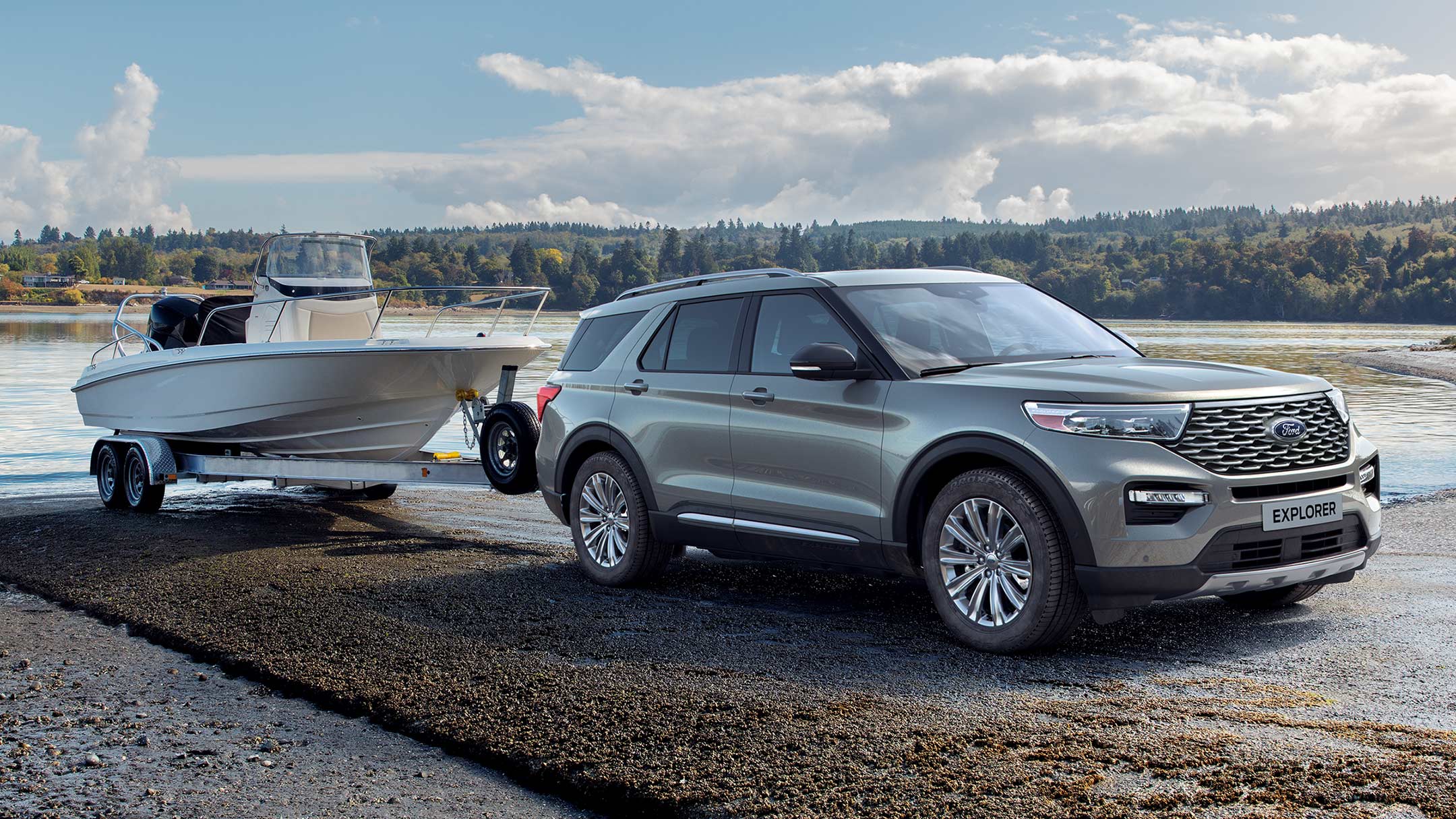 Ford Explorer Plug-In Hybrid couleur argent. Vue de face aux trois quarts. Avec une remorque à bateaux au bord d’un lac