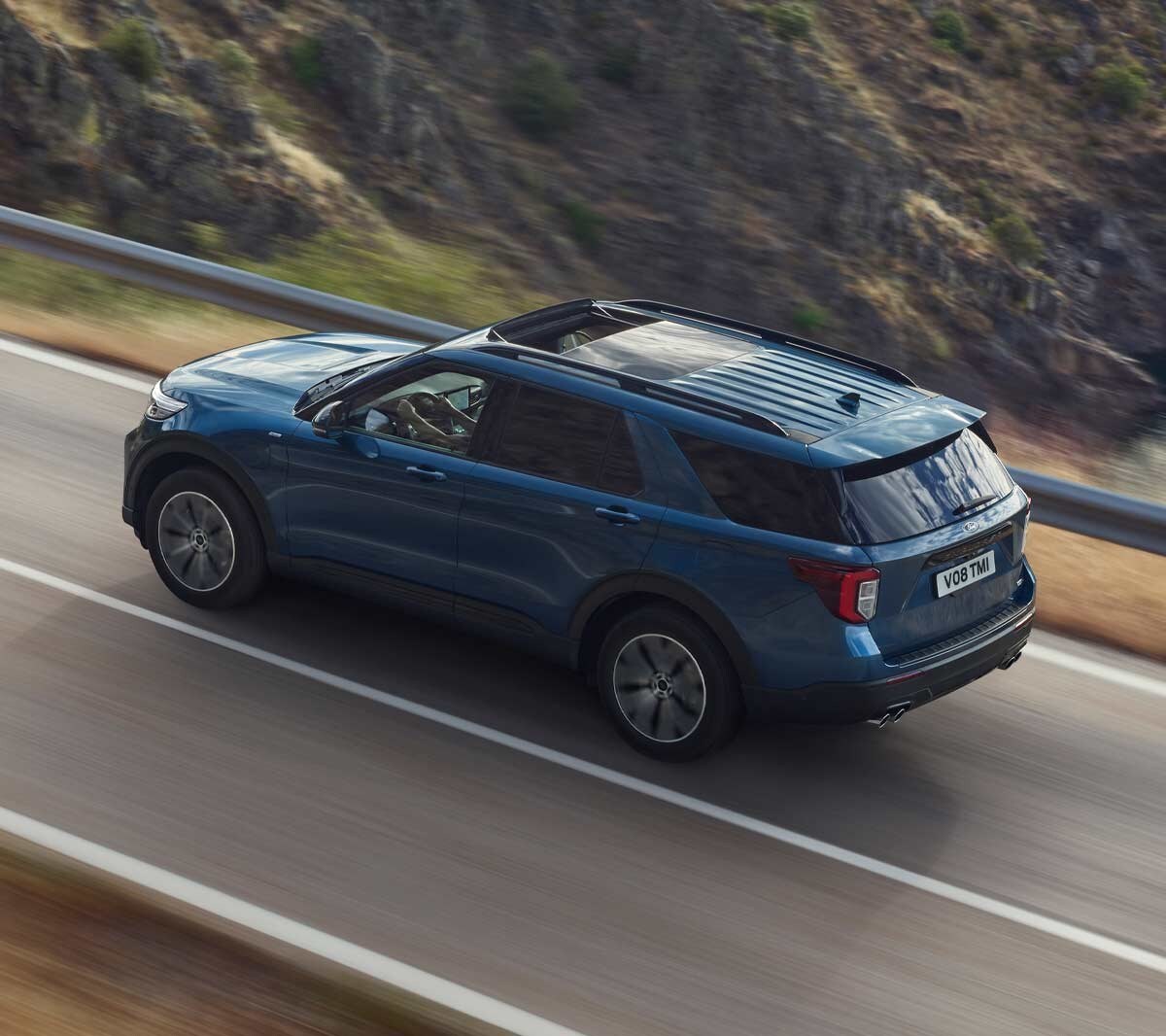 Ford Explorer Plug-In Hybrid bleu. Vue trois-quarts arrière. Conduite sur une route de montagne