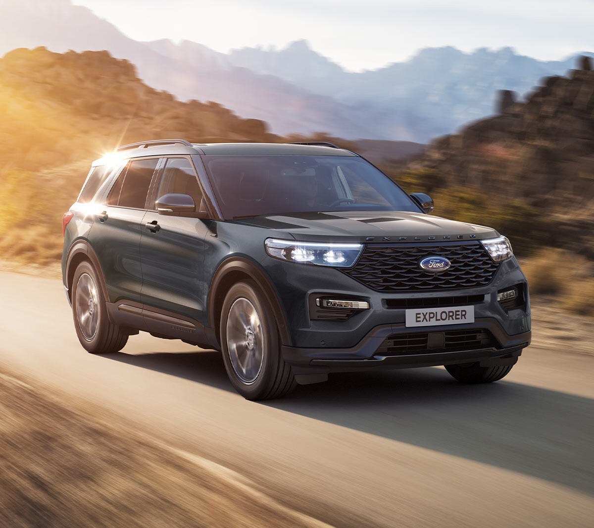 Ford Explorer Plug-In Hybrid couleur bleue. Vue de face aux trois quarts. Scène de conduite sur une route de campagne avec des montagnes en arrière-plan