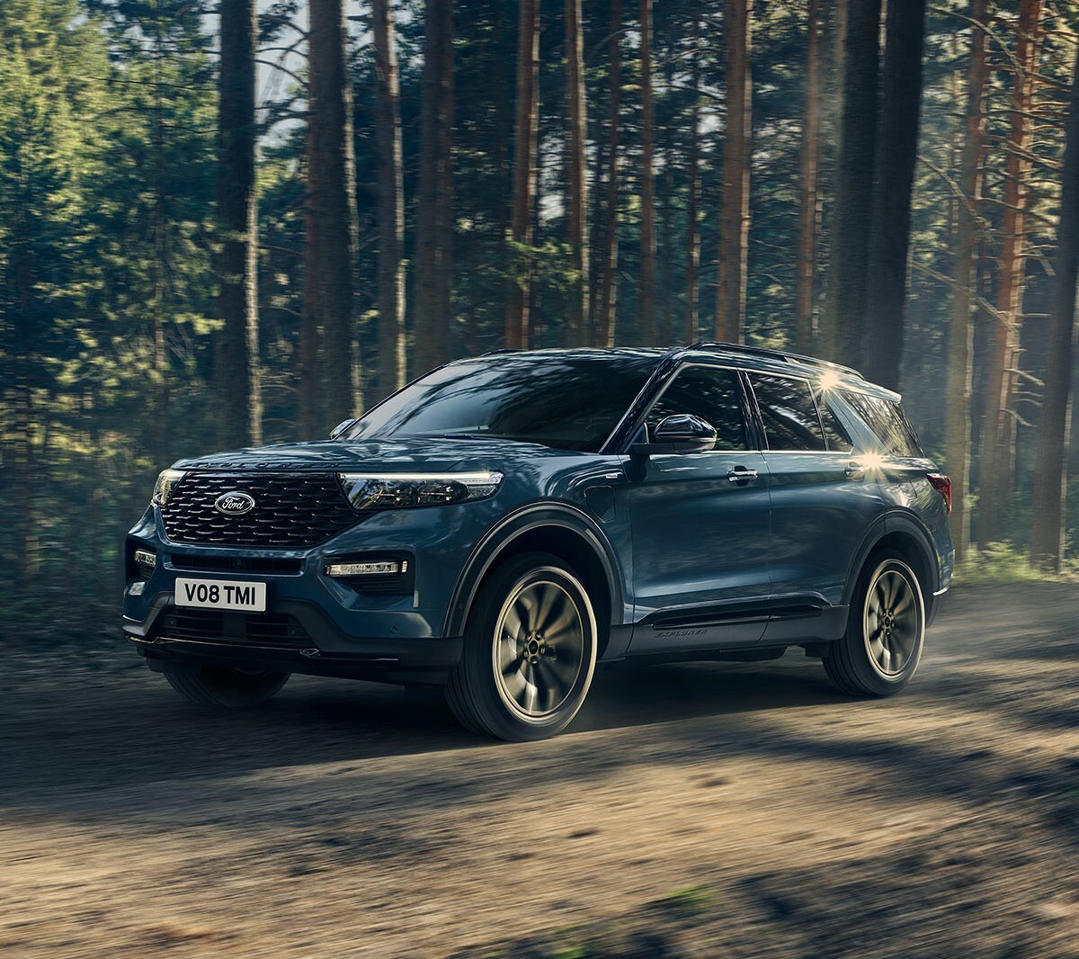 Ford Explorer Plug-In Hybrid bleu. Vue trois-quarts avant. Conduite sur une route de campagne avec une forêt en arrière-plan 