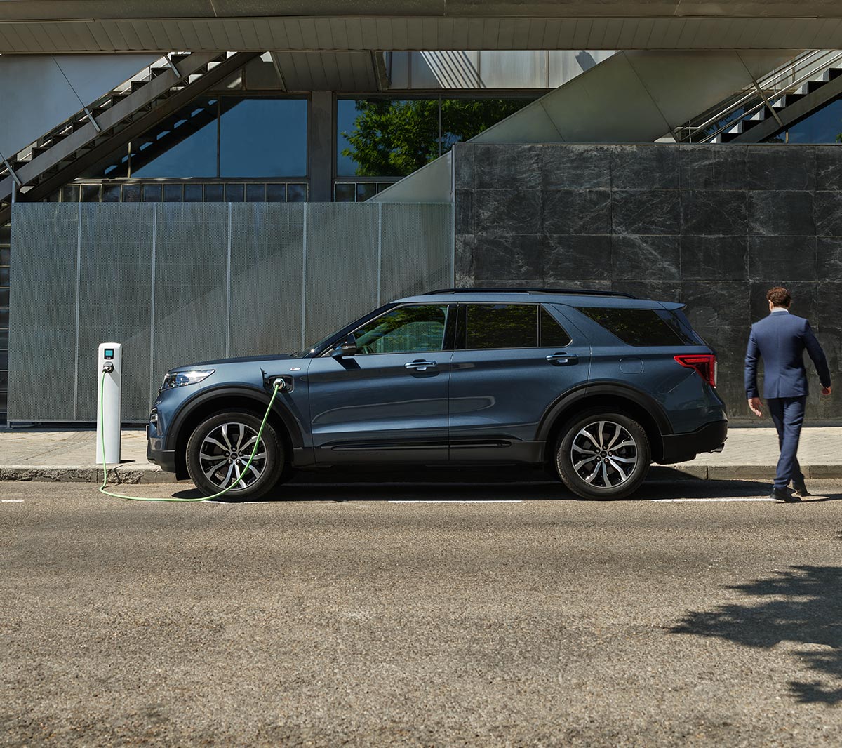 Ford Explorer Plug-In Hybrid bleu. Vue latérale. Stationnement à une station de charge