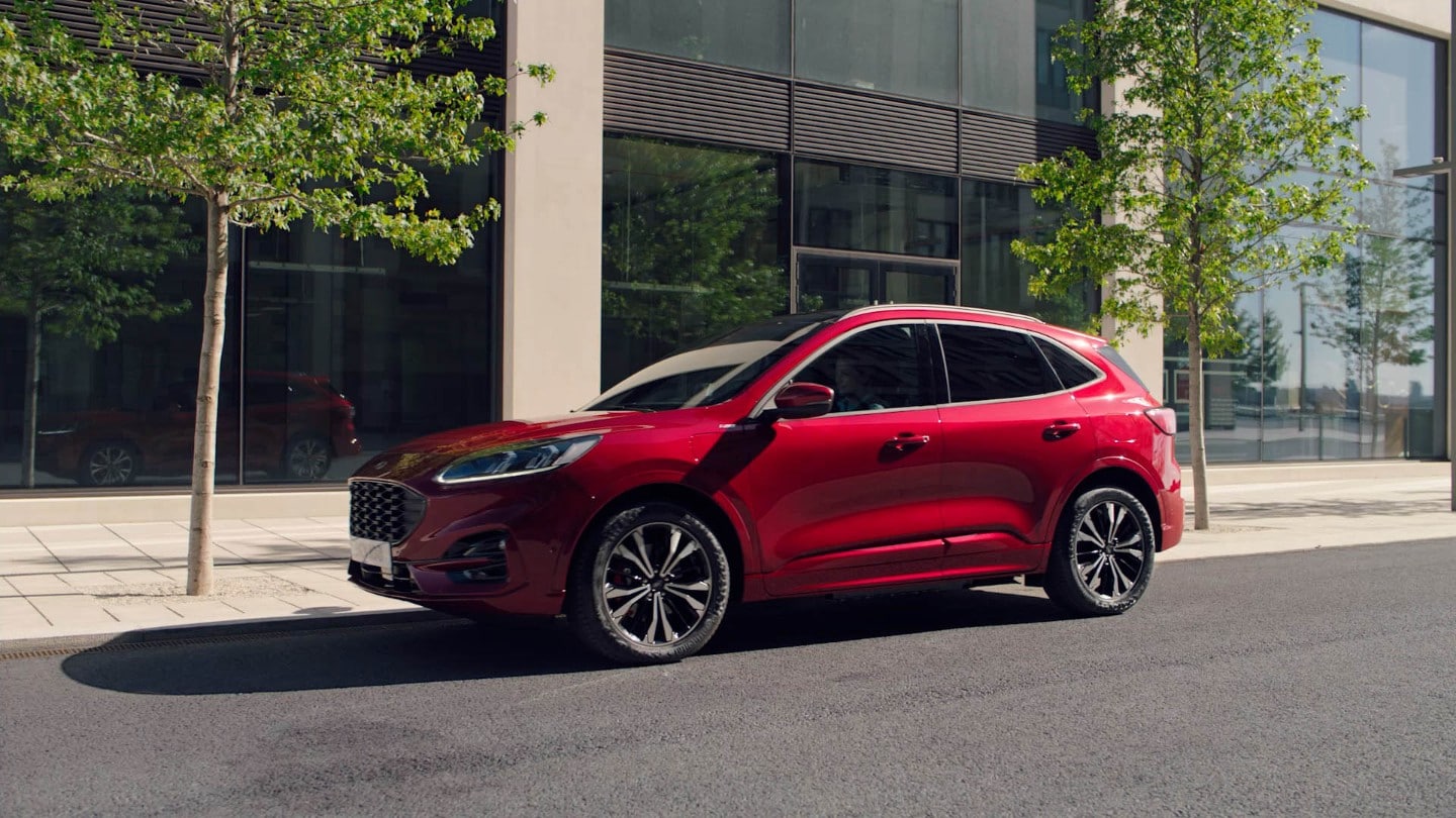 Ford Kuga Plug-in Hybrid (PHEV) couleur rouge. Vue latérale, garé devant un bâtiment moderne