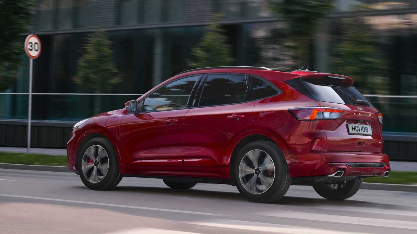 Ford Kuga couleur rouge. Vue latérale, roulant sur une route