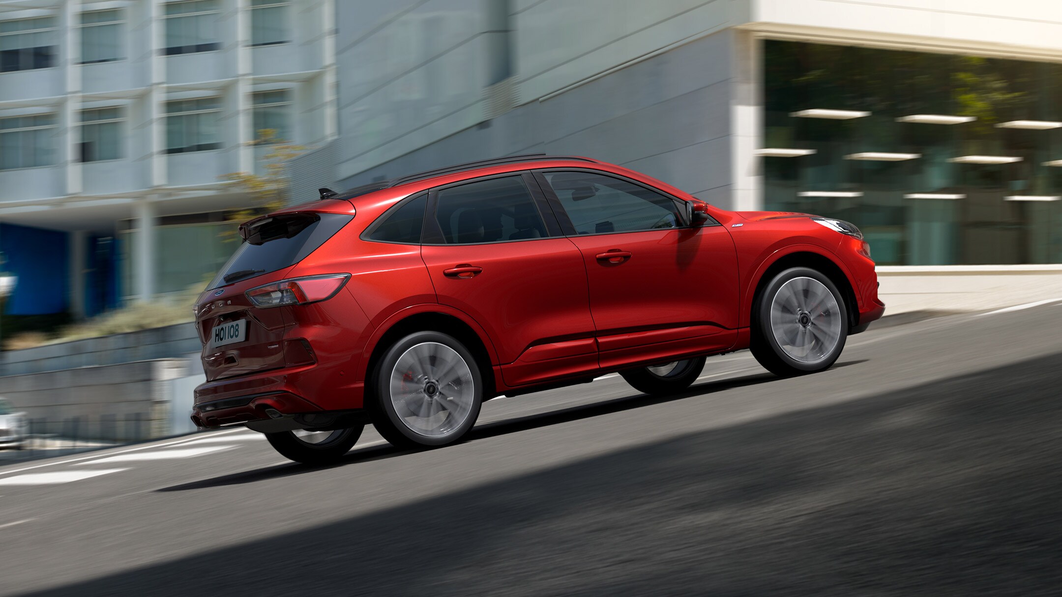 Ford Kuga couleur rouge. Vue latérale, roulant dans une pente en ville