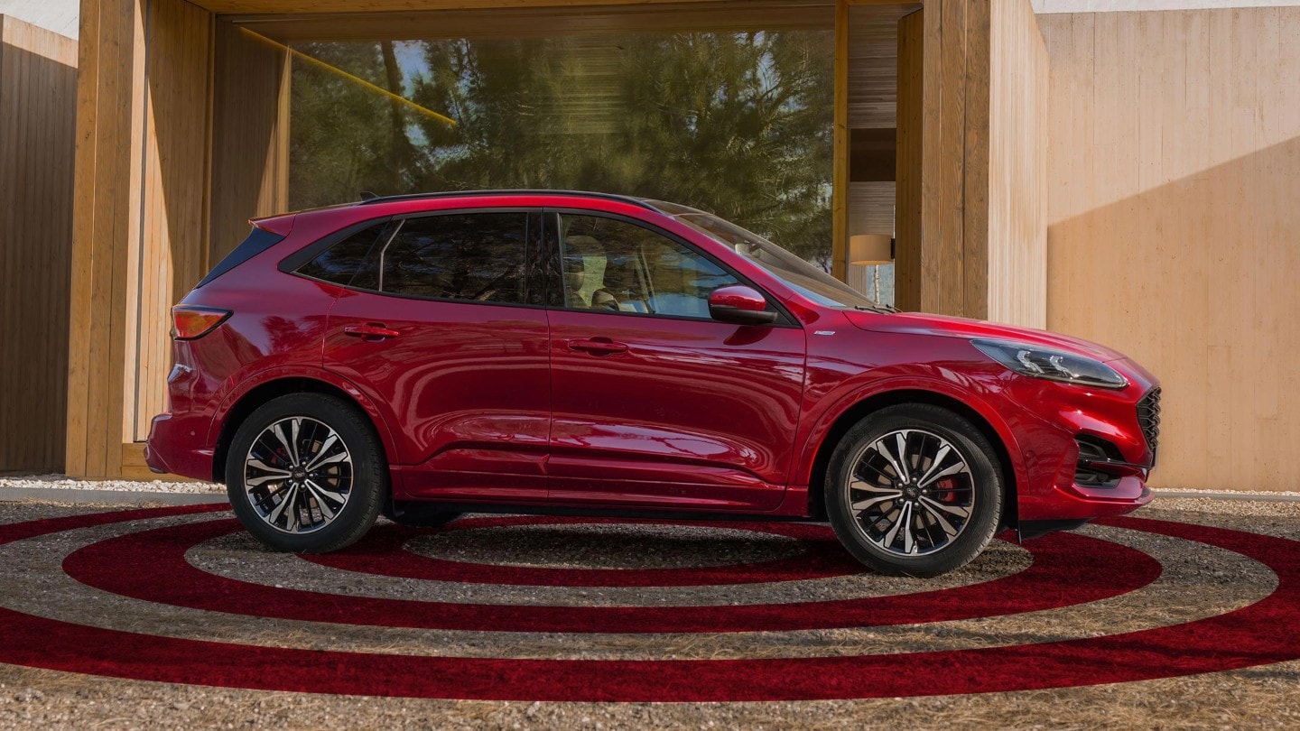 Ford Kuga couleur rouge. Vue latérale, garé devant un bâtiment moderne