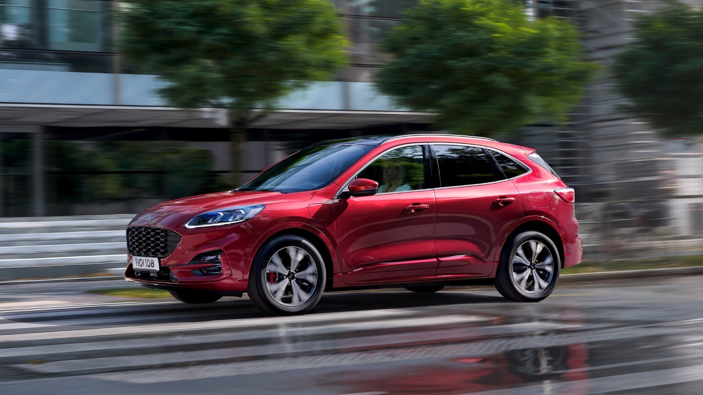 Ford Kuga couleur rouge. Vue latérale, roulant devant un passage pour piétons en ville