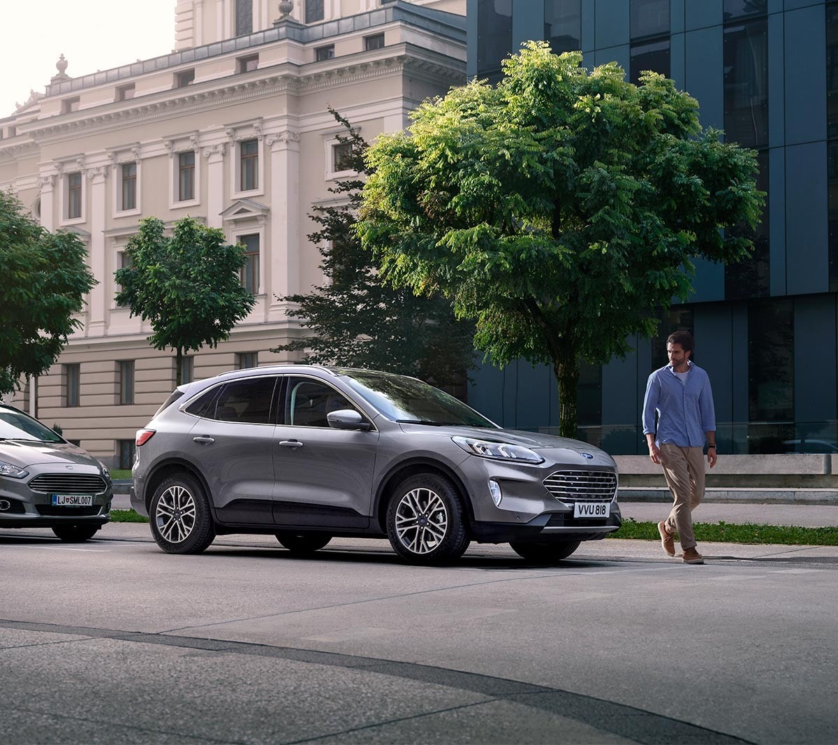 Ford Kuga couleur grise. Vue de face aux trois quarts, garé devant un bâtiment ancien